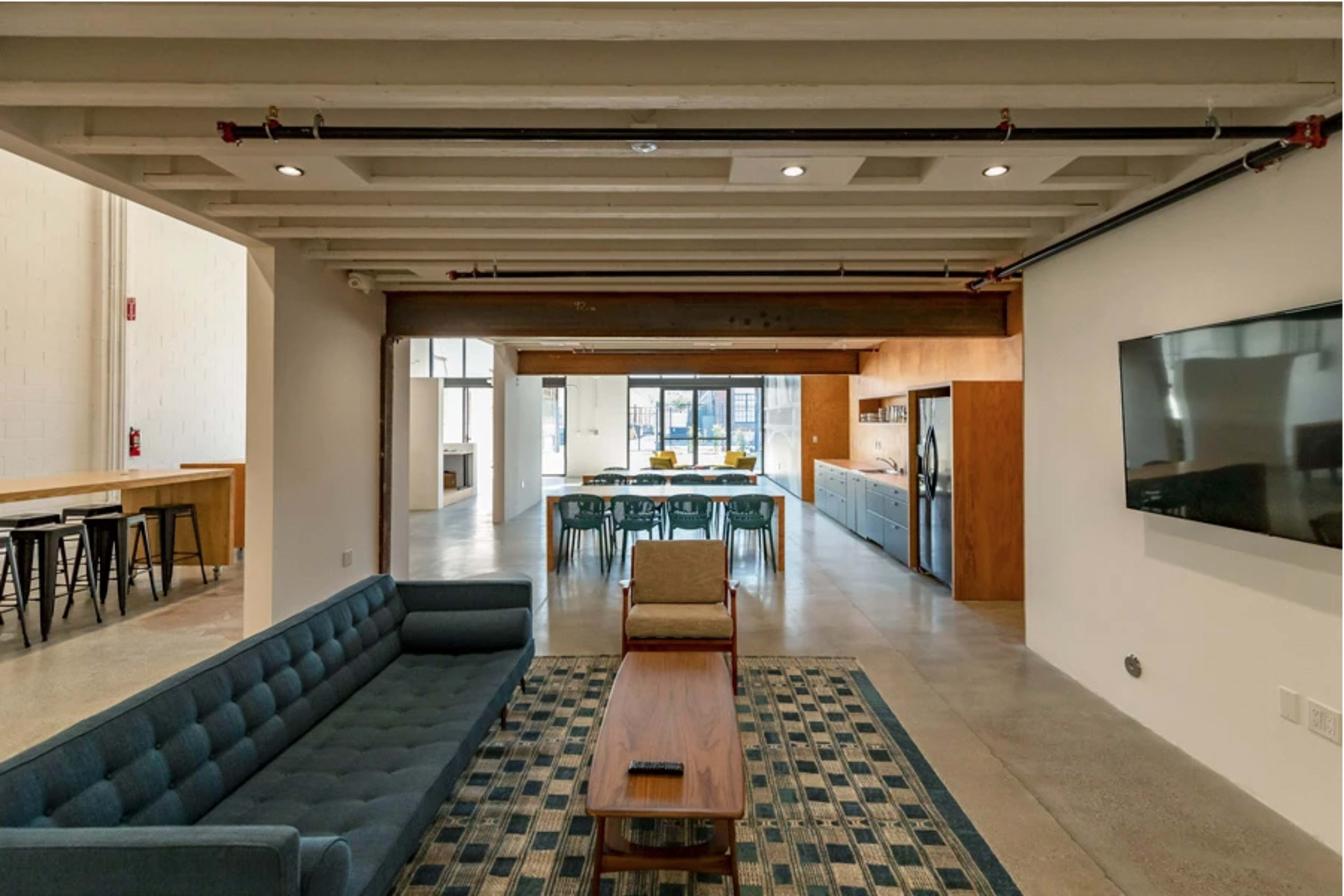 A modern open-concept living space featuring a blue sofa, wooden coffee table, and a dining area with a long table and chairs in the background.