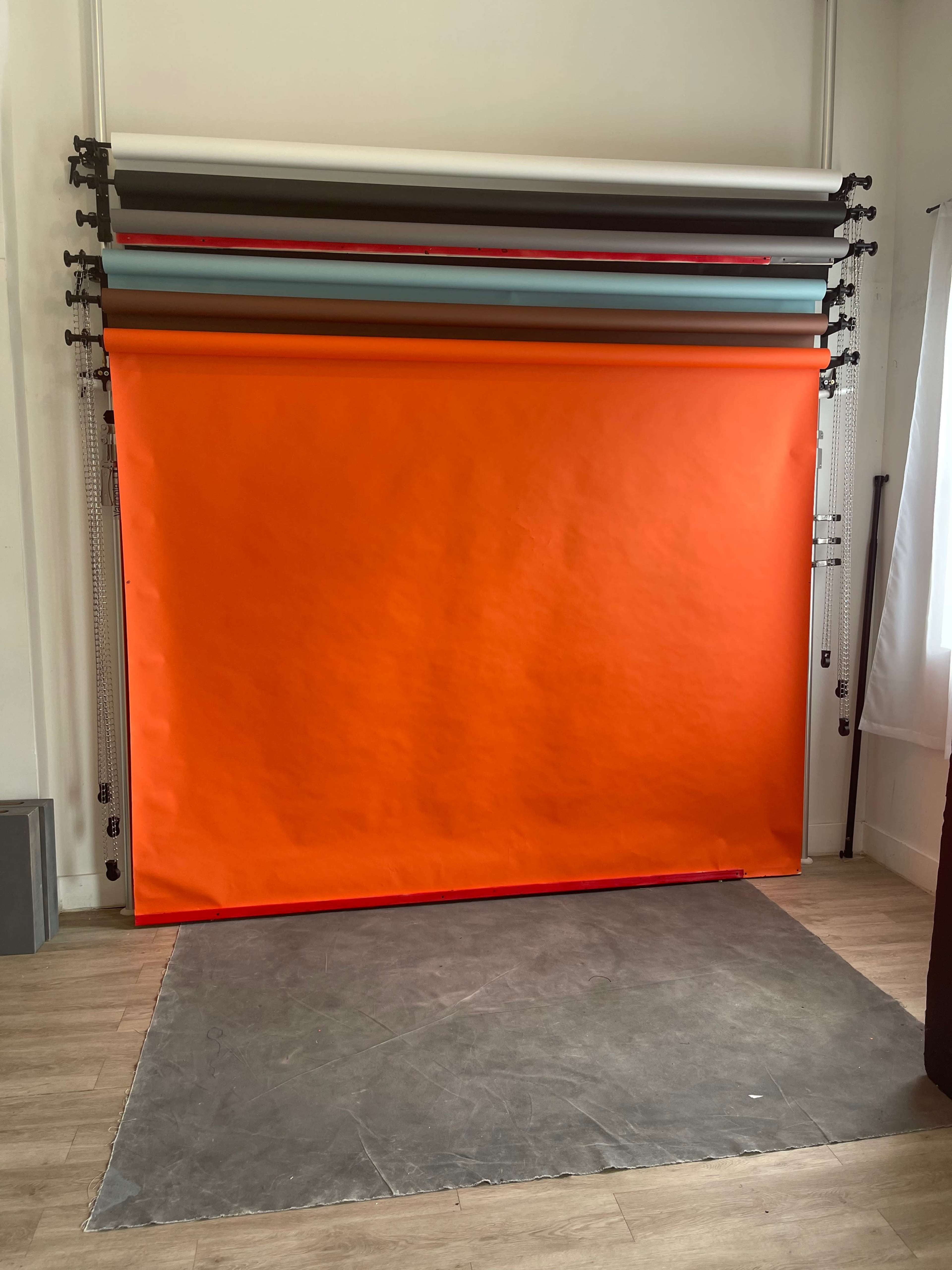 A photography studio setup with a bright orange backdrop and several rolls of colored paper hanging above it.