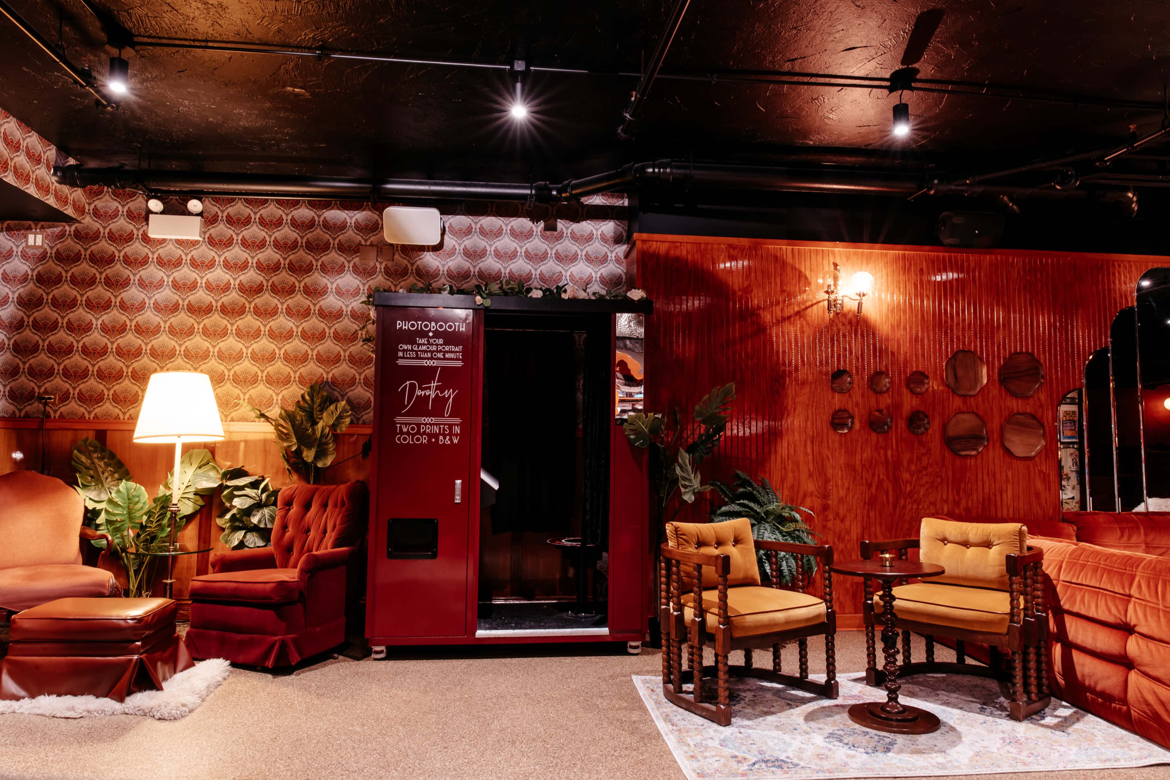 The scene features a cozy seating area with vintage furniture, including a red photobooth and decorative wall patterns.