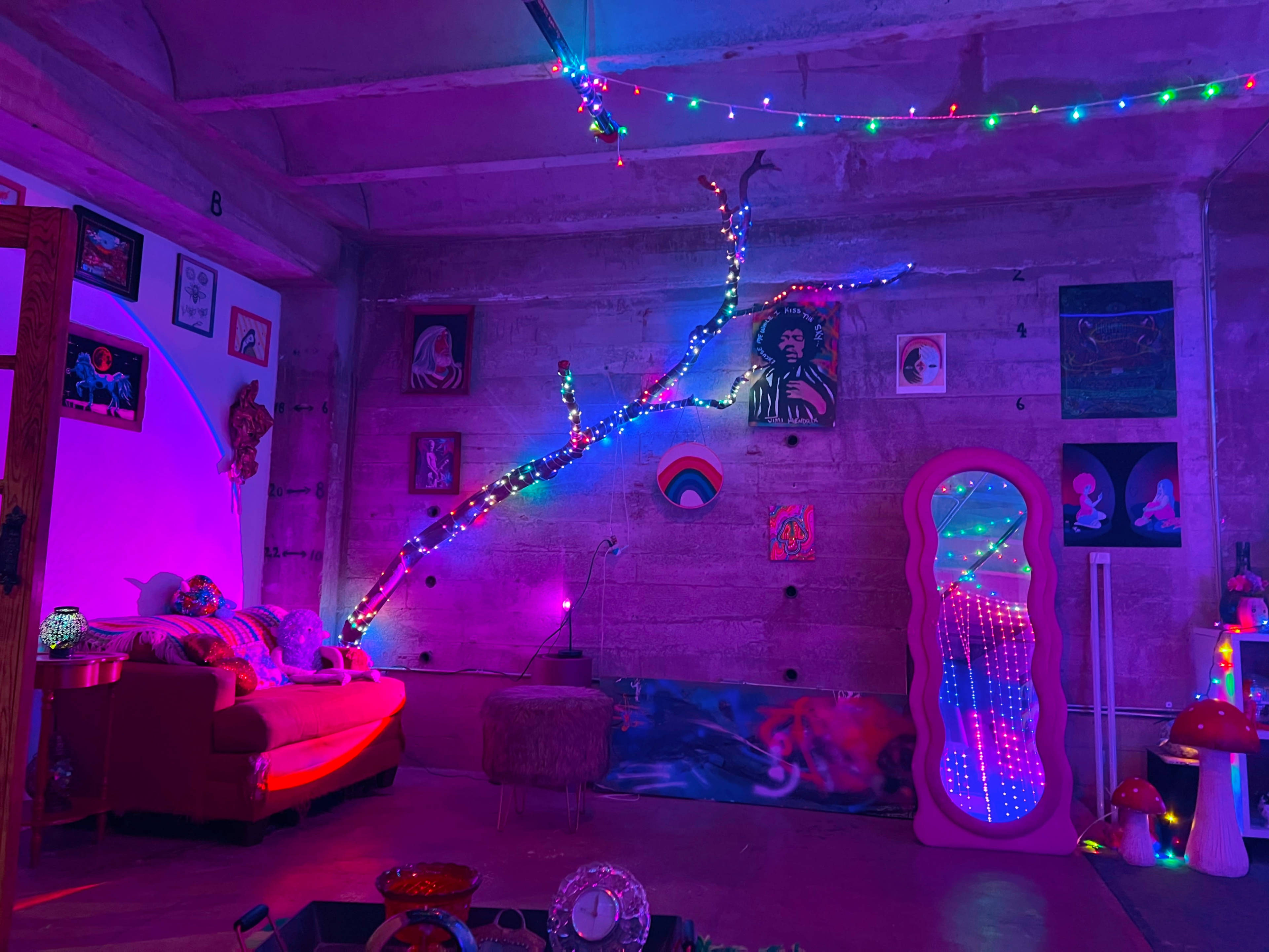 The image shows a colorful room with a couch, illuminated by string lights and various artwork hanging on the walls.