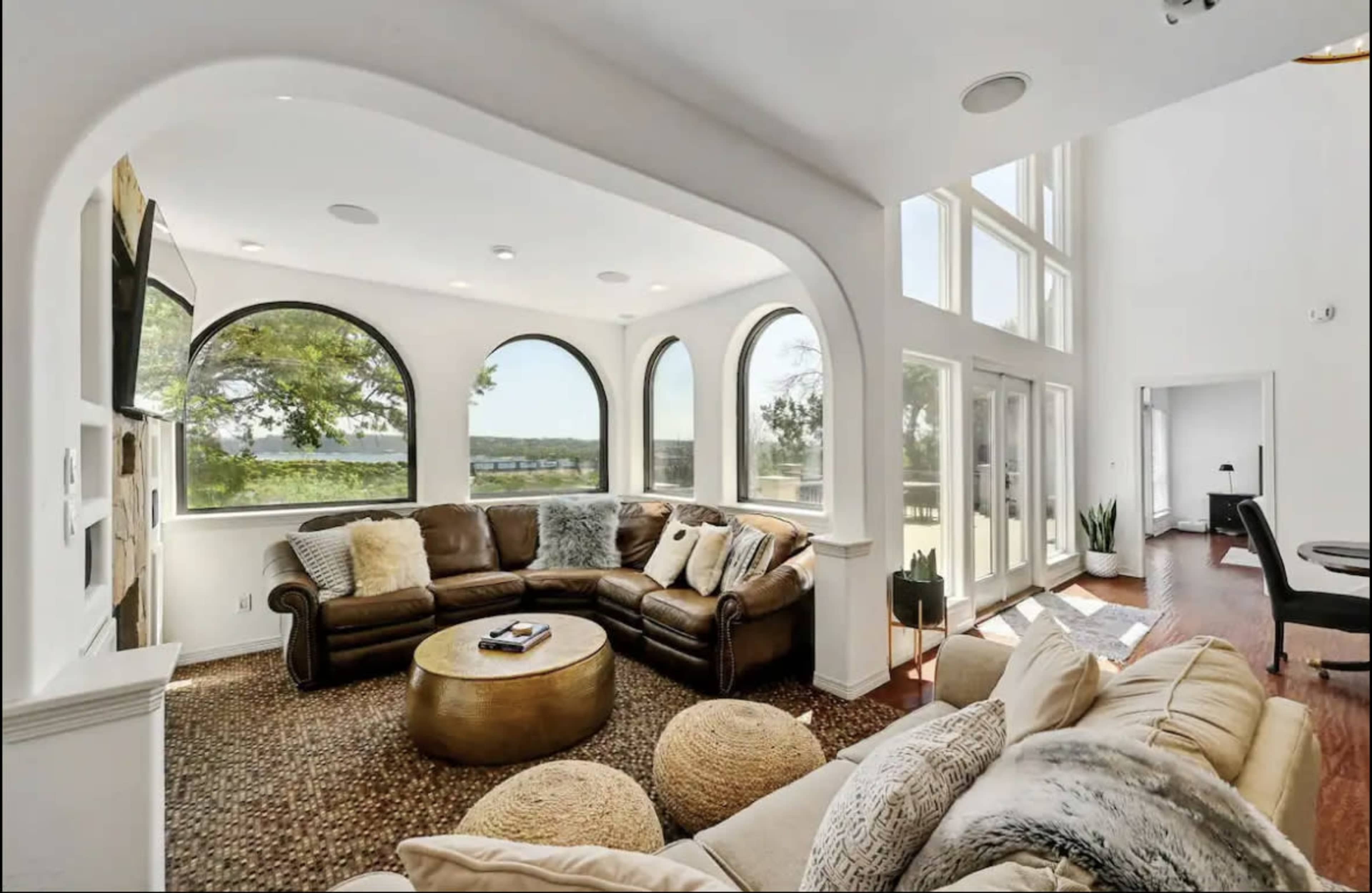 A spacious living room with large arched windows, two seating areas, and a view of a landscape outside.