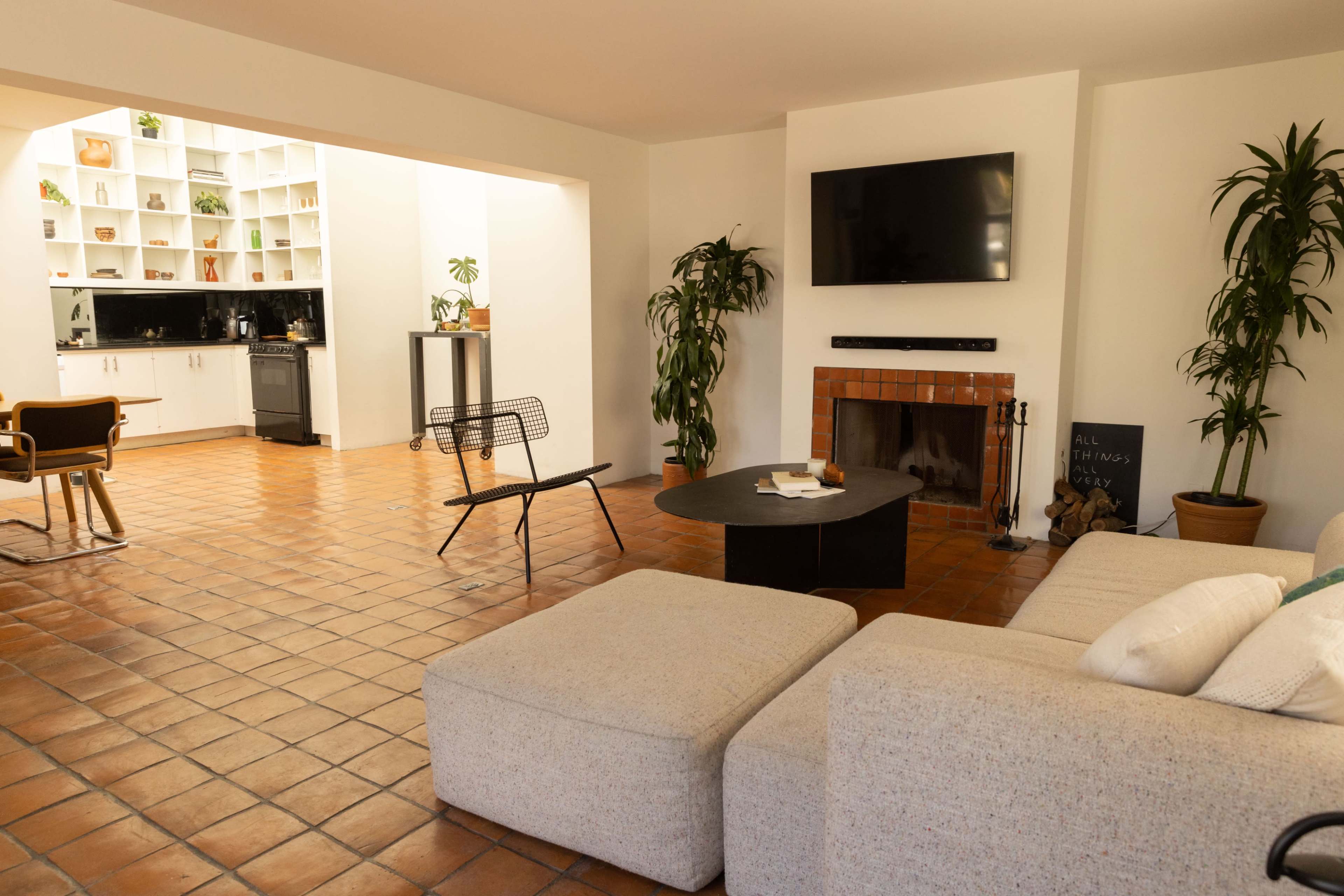 A spacious living area features a sectional sofa, a round coffee table, a fireplace, and a view into a kitchen with a black countertop and white cabinetry.