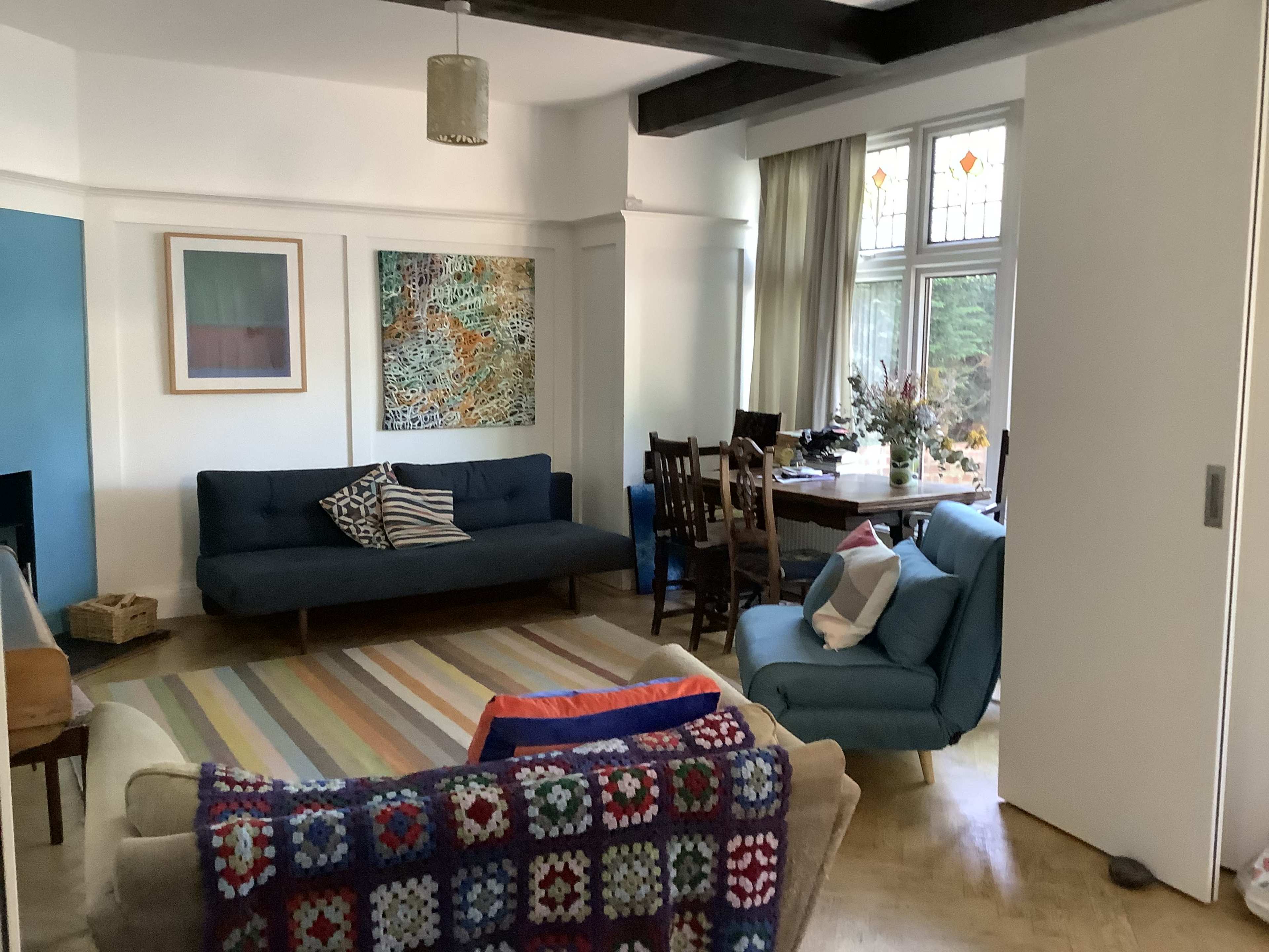 A cozy living room with a blue sofa, a light-colored armchair, a patterned rug, and a dining table set for several people.