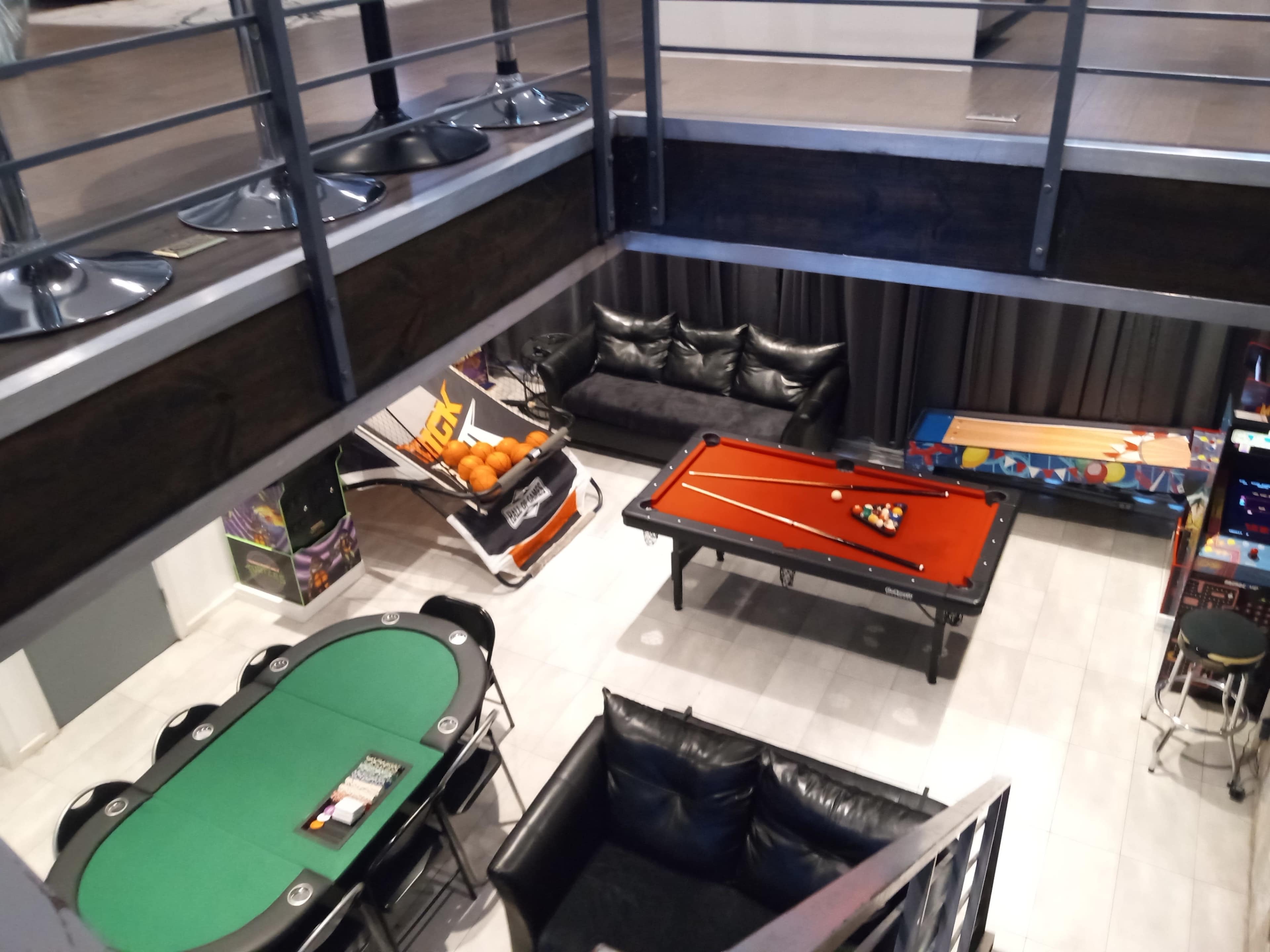 The image shows a recreation room with a pool table, a poker table, a couch area, and arcade games.