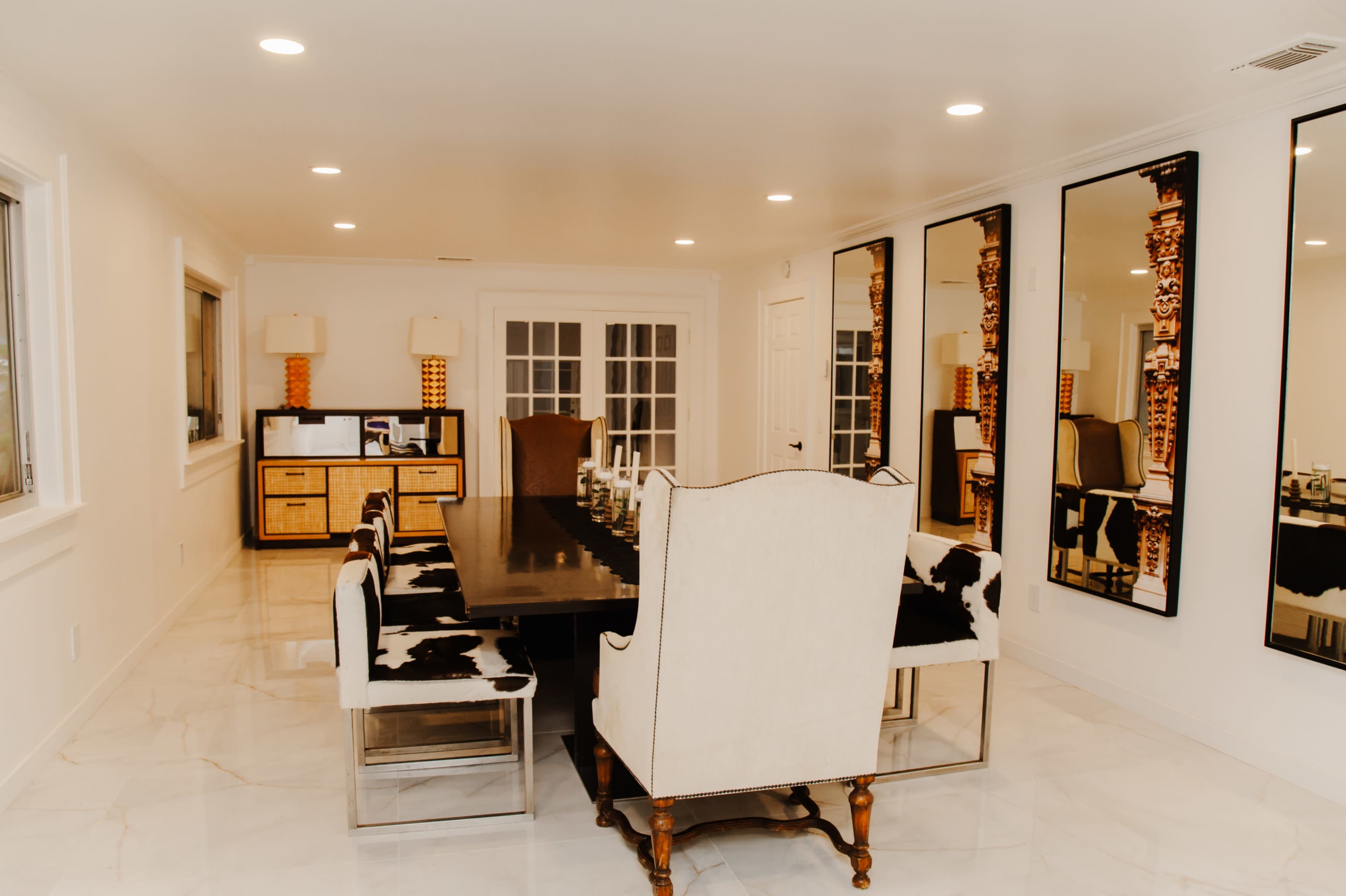 A modern dining room featuring a long black table surrounded by upholstered chairs and large mirrors on the walls.