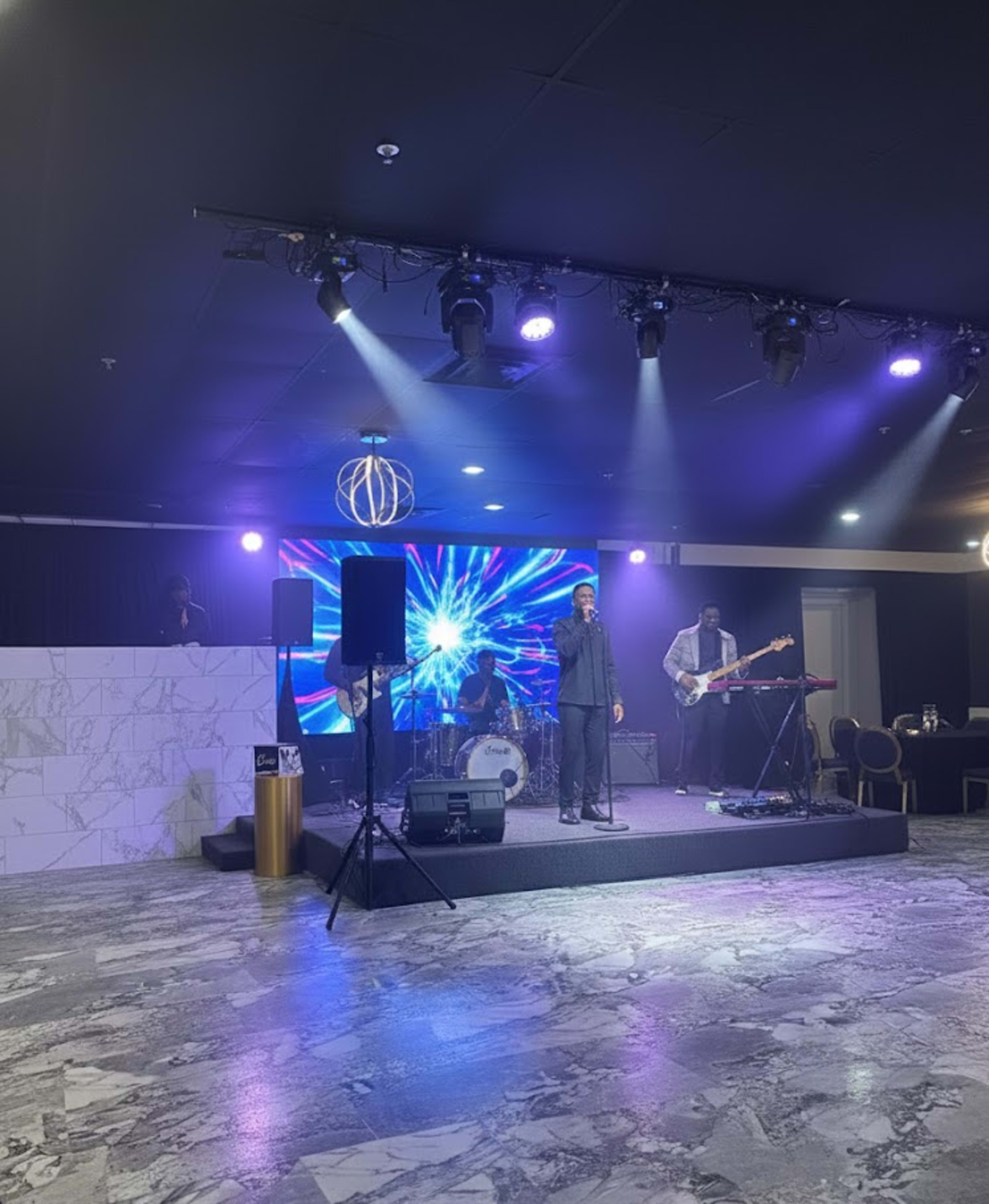 A band performs on a stage equipped with vibrant lighting and a large screen displaying colorful graphics.