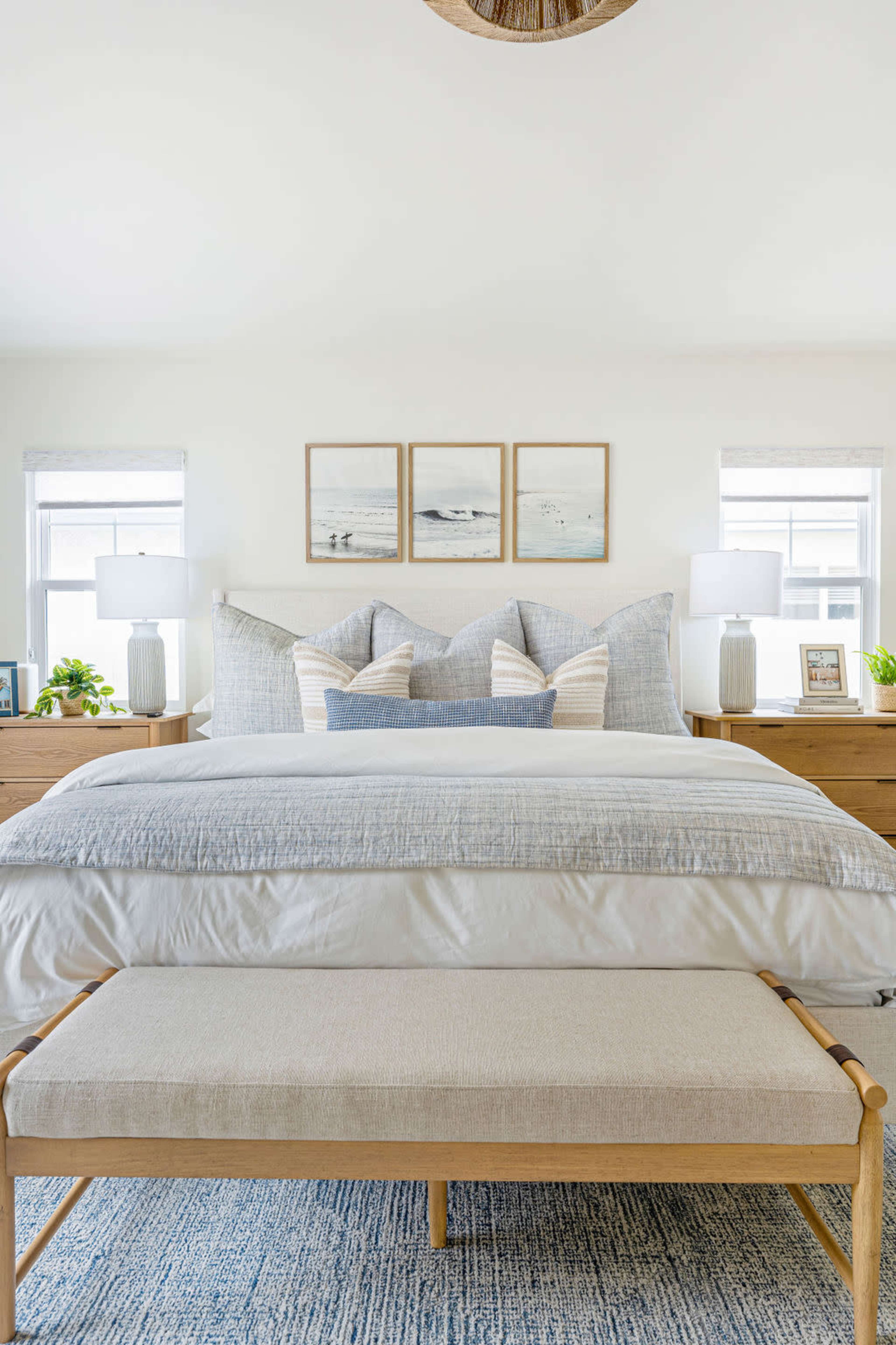 A bright and modern bedroom features a bed with layered bedding, decorative pillows, bedside tables with lamps, and framed artwork on the wall.
