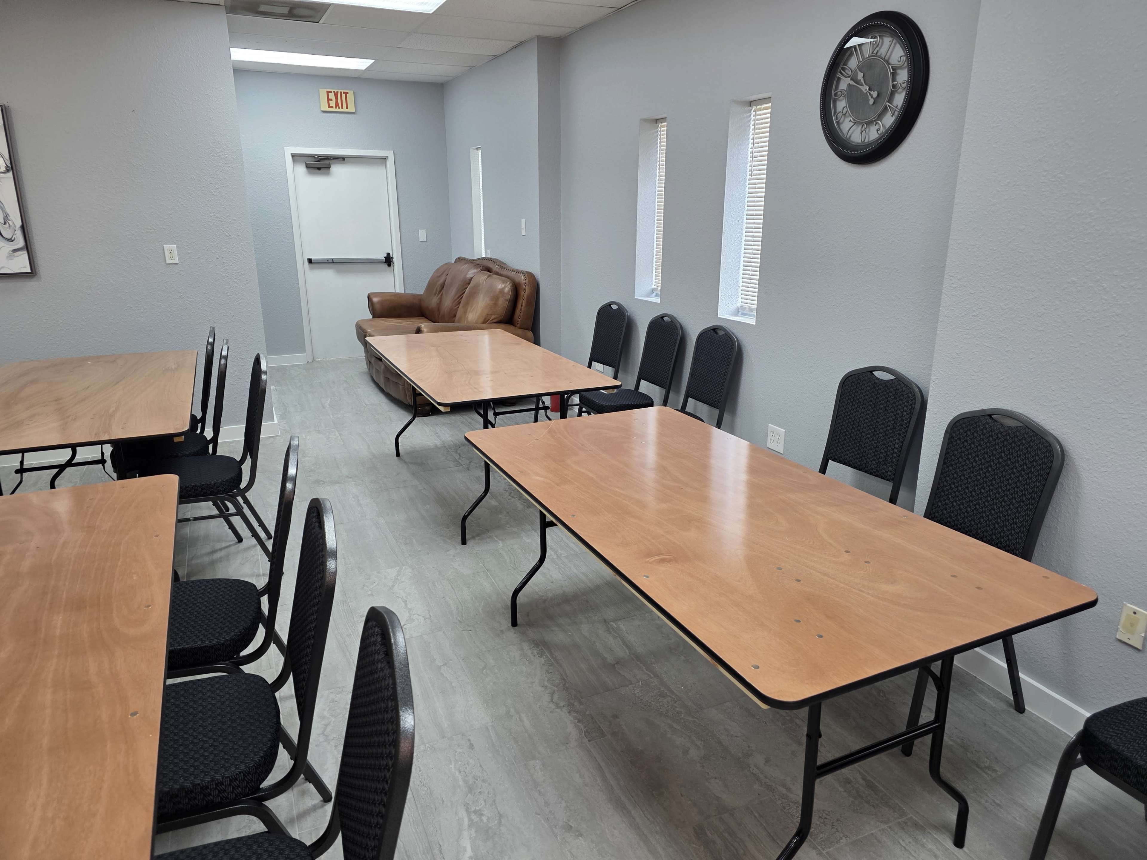 The image shows a room with two sets of tables and chairs arranged in a rectangular layout, along with a sofa and a wall clock visible in the background.