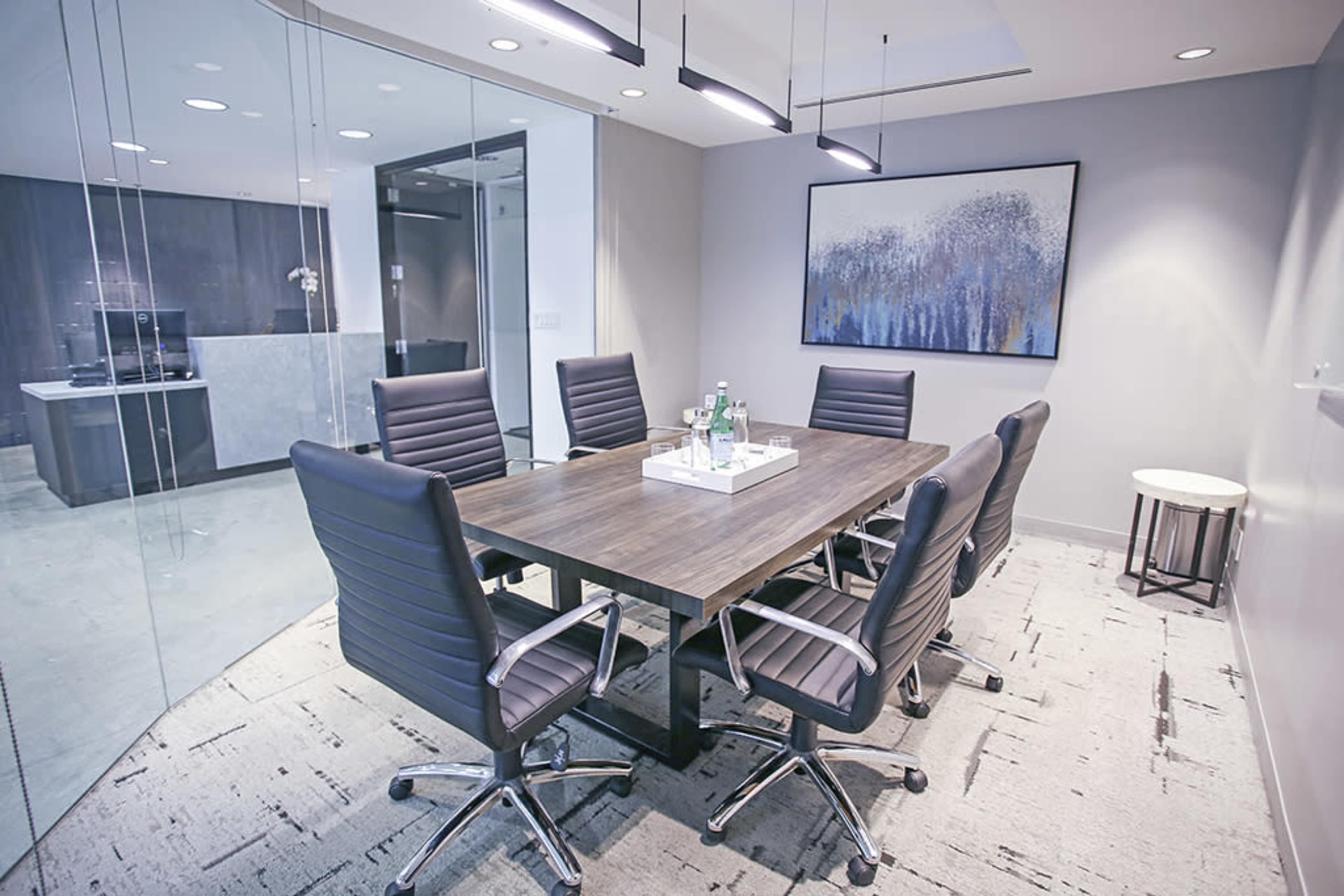 A modern conference room features a large wooden table surrounded by black ergonomic chairs, with glass walls offering a view of an adjacent space.