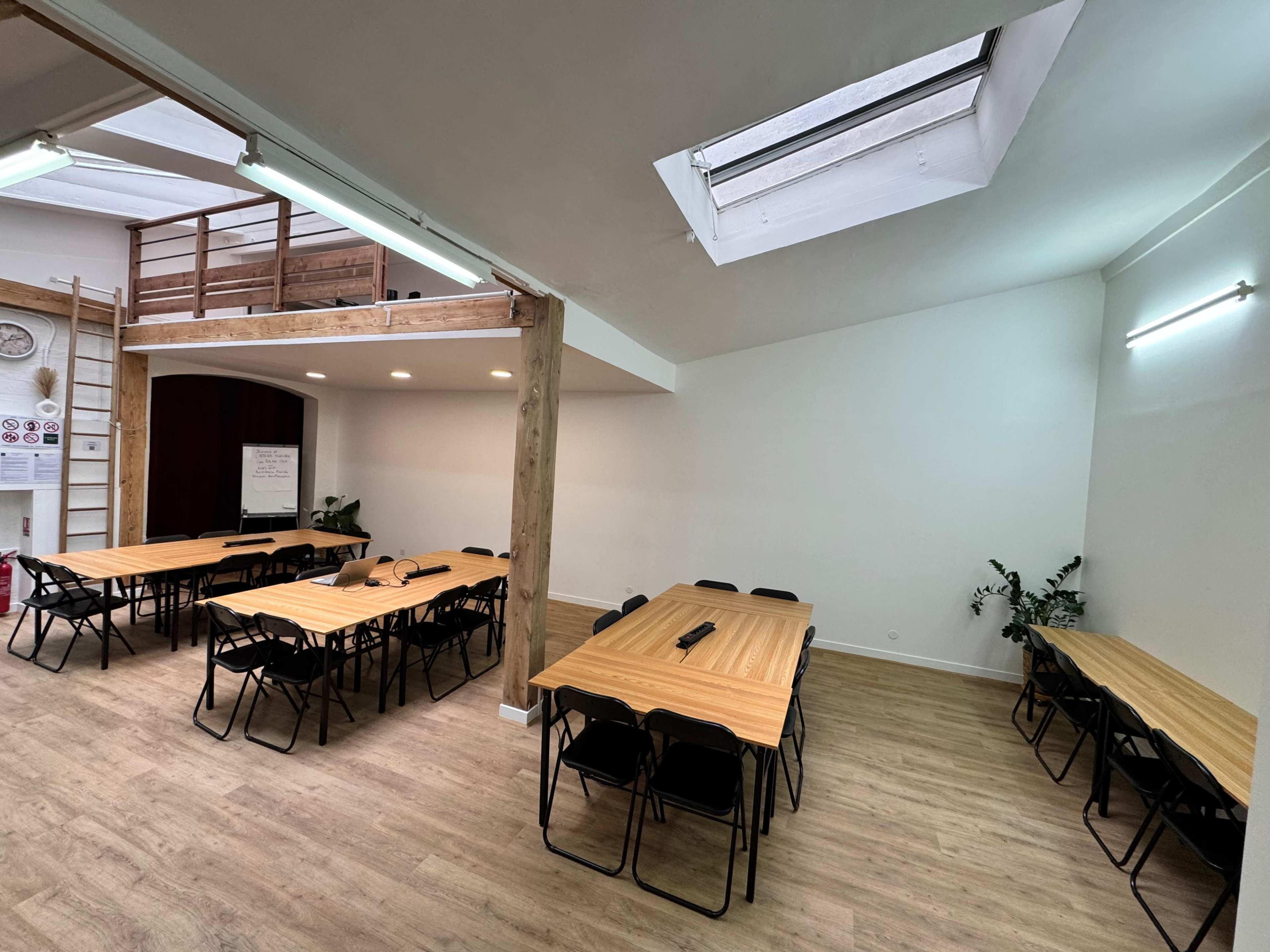 The image shows a spacious, well-lit meeting room with several wooden tables arranged in rows and black chairs along the sides.