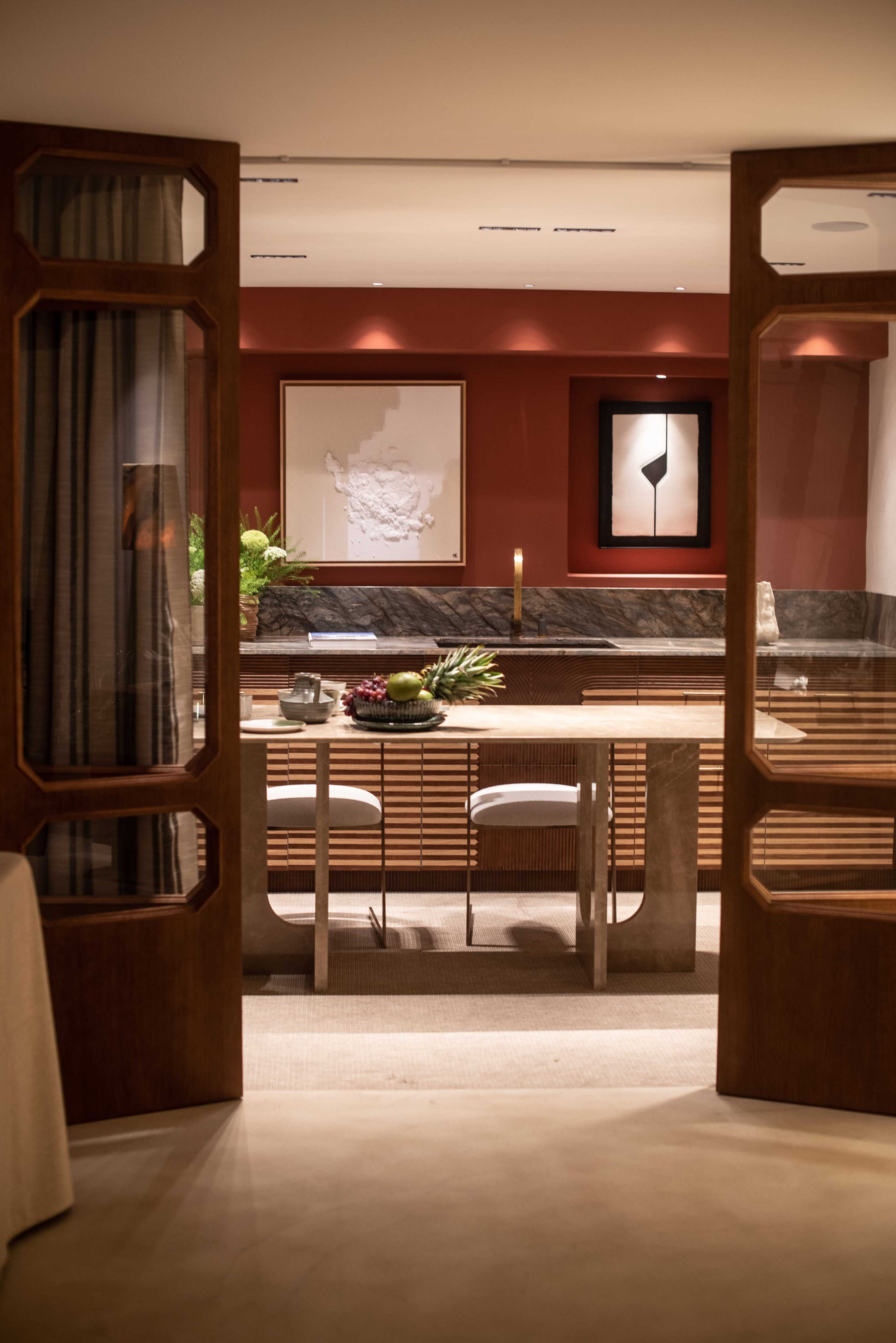 The image shows an elegantly designed interior space featuring a modern reception area with wooden doors opened to reveal a countertop and art pieces on the walls.