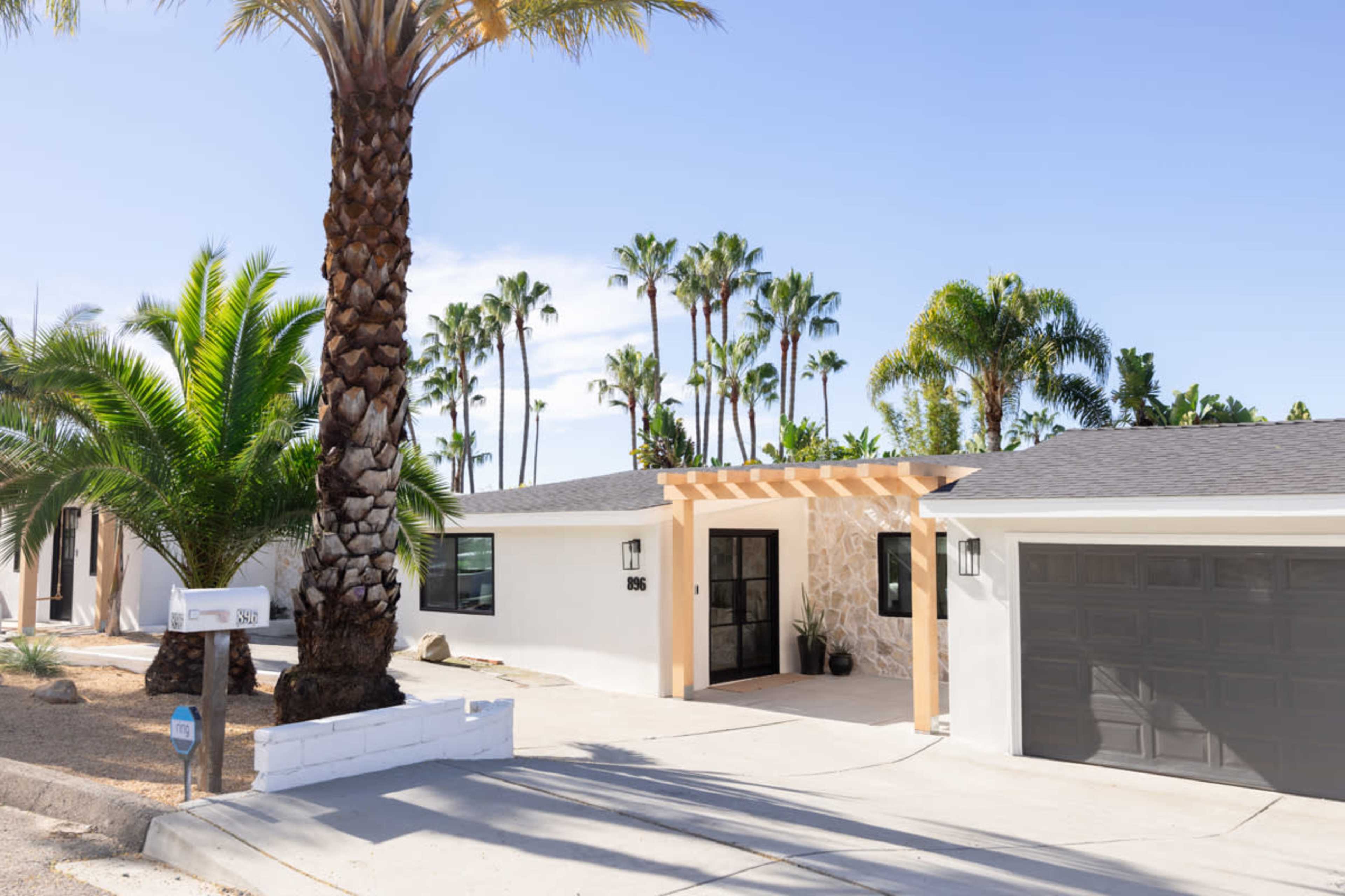 A modern single-story house with a stone facade, palm trees, and a driveway leading to a garage.