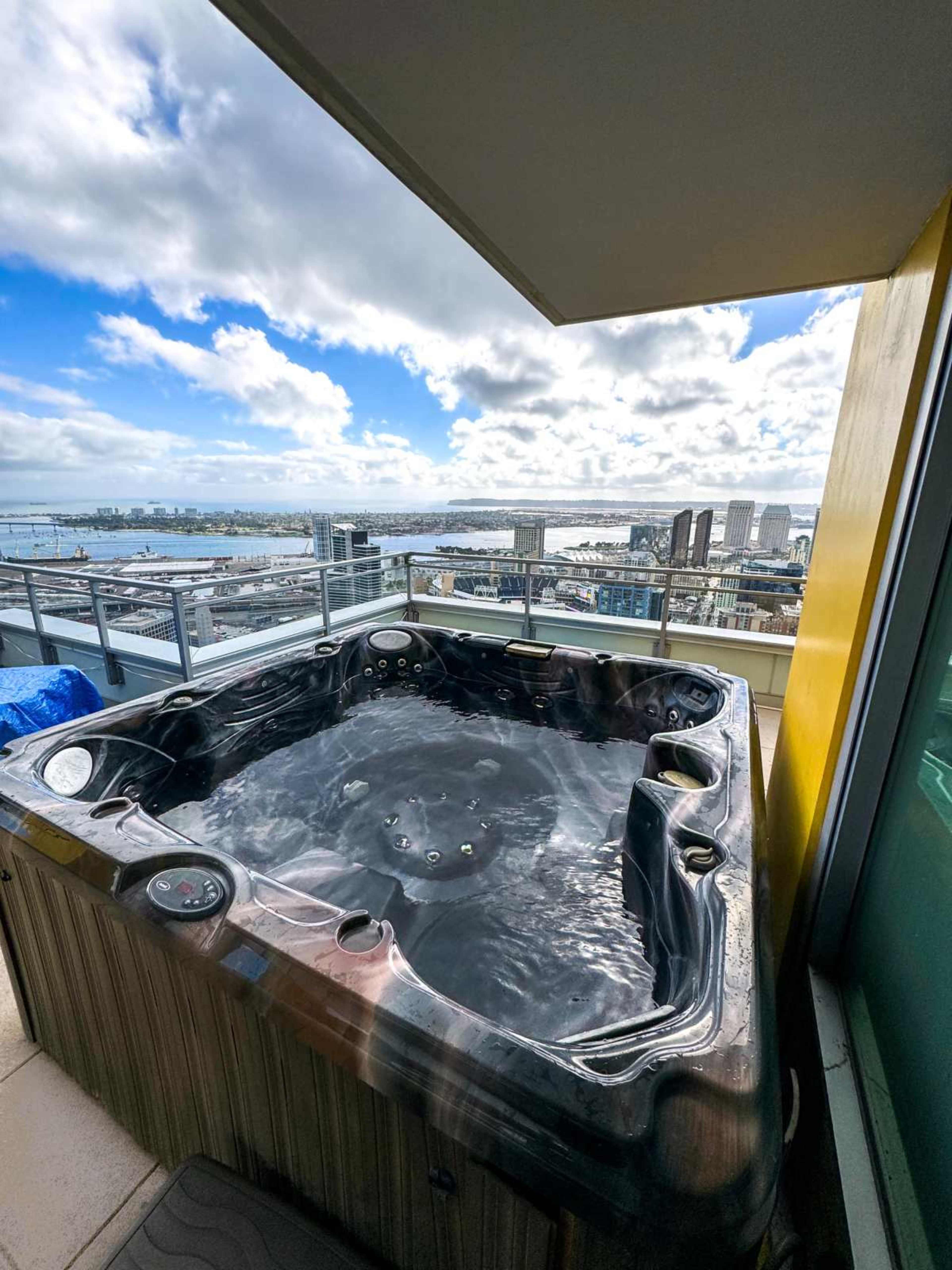 A hot tub sits on a balcony with a panoramic view of a cityscape and water.