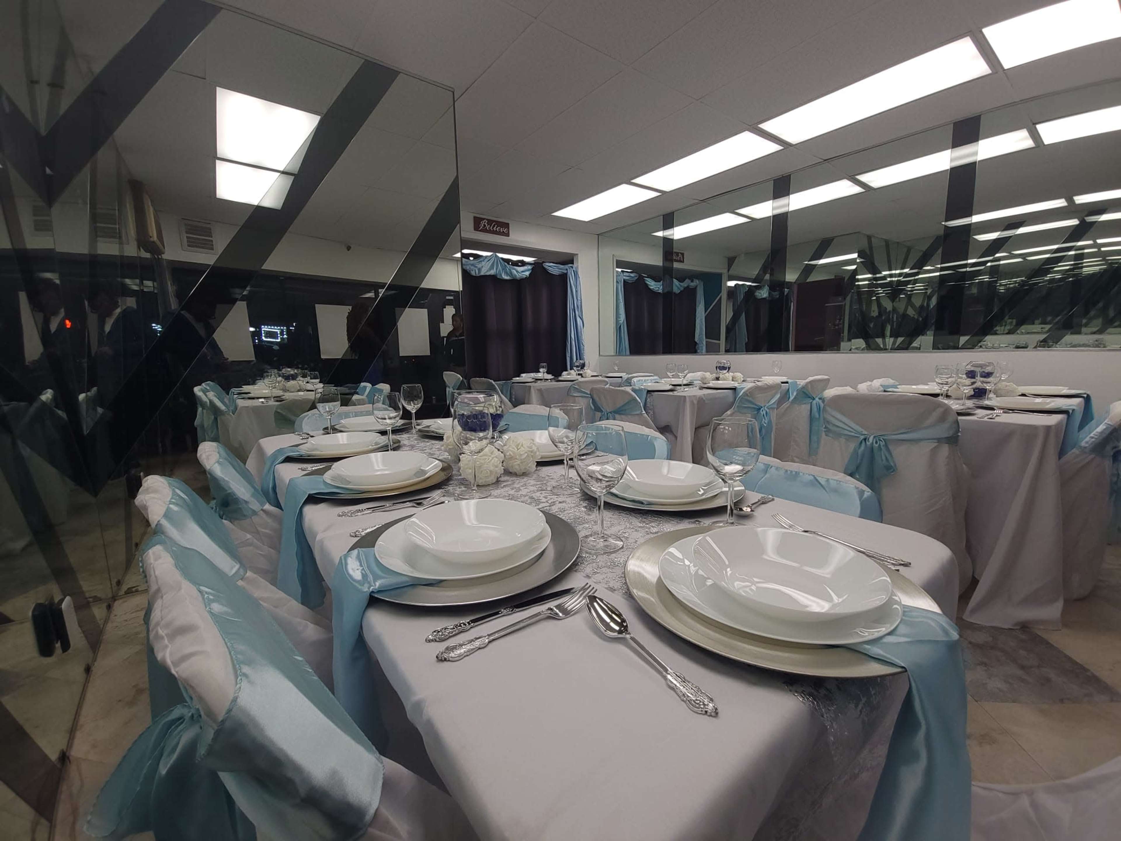 A dining area set with elegantly arranged tables covered in white tablecloths and decorated with light blue accents.