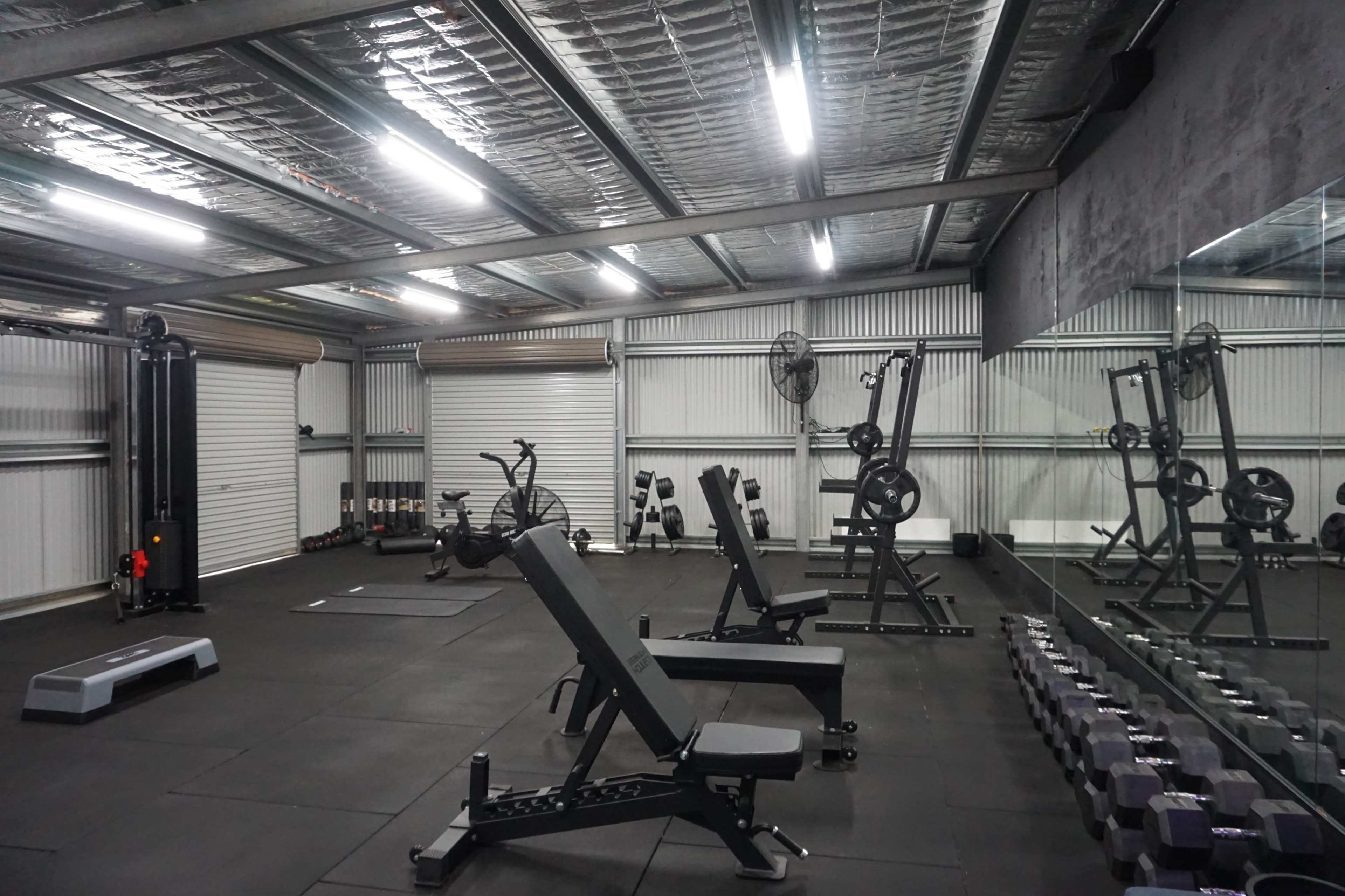 A spacious gym with various exercise equipment, including benches, weights, and cardio machines, arranged in a well-lit area.