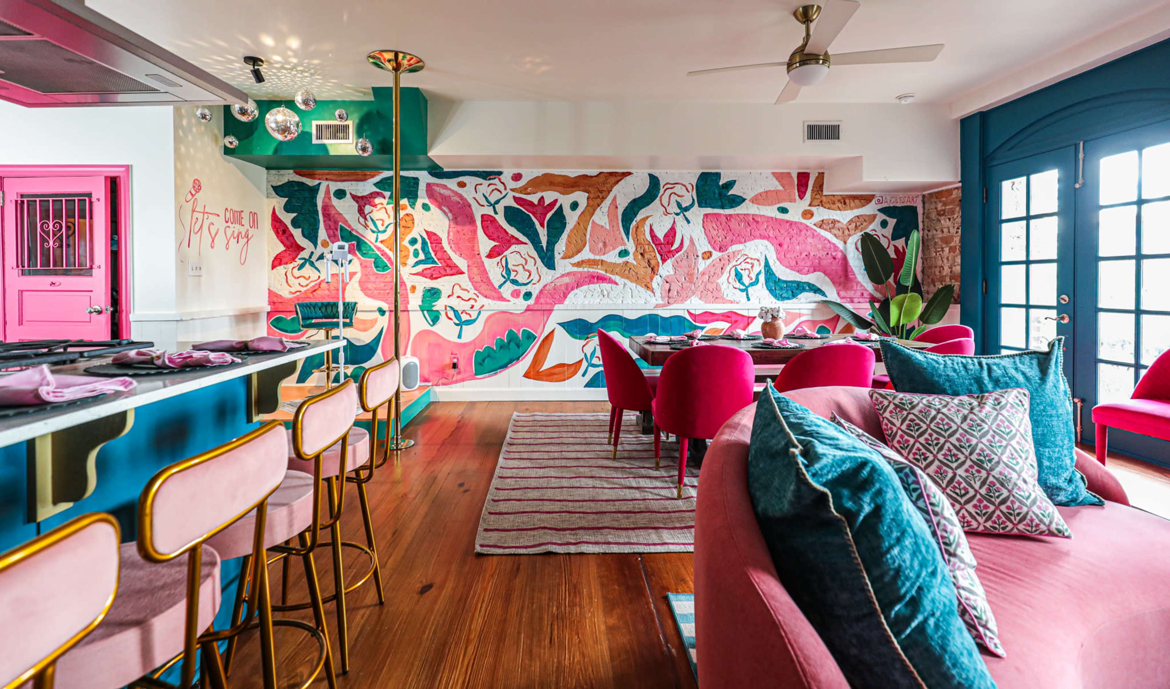 A colorful, modern interior space featuring a vibrant mural, stylish seating, and a bar with golden accents.