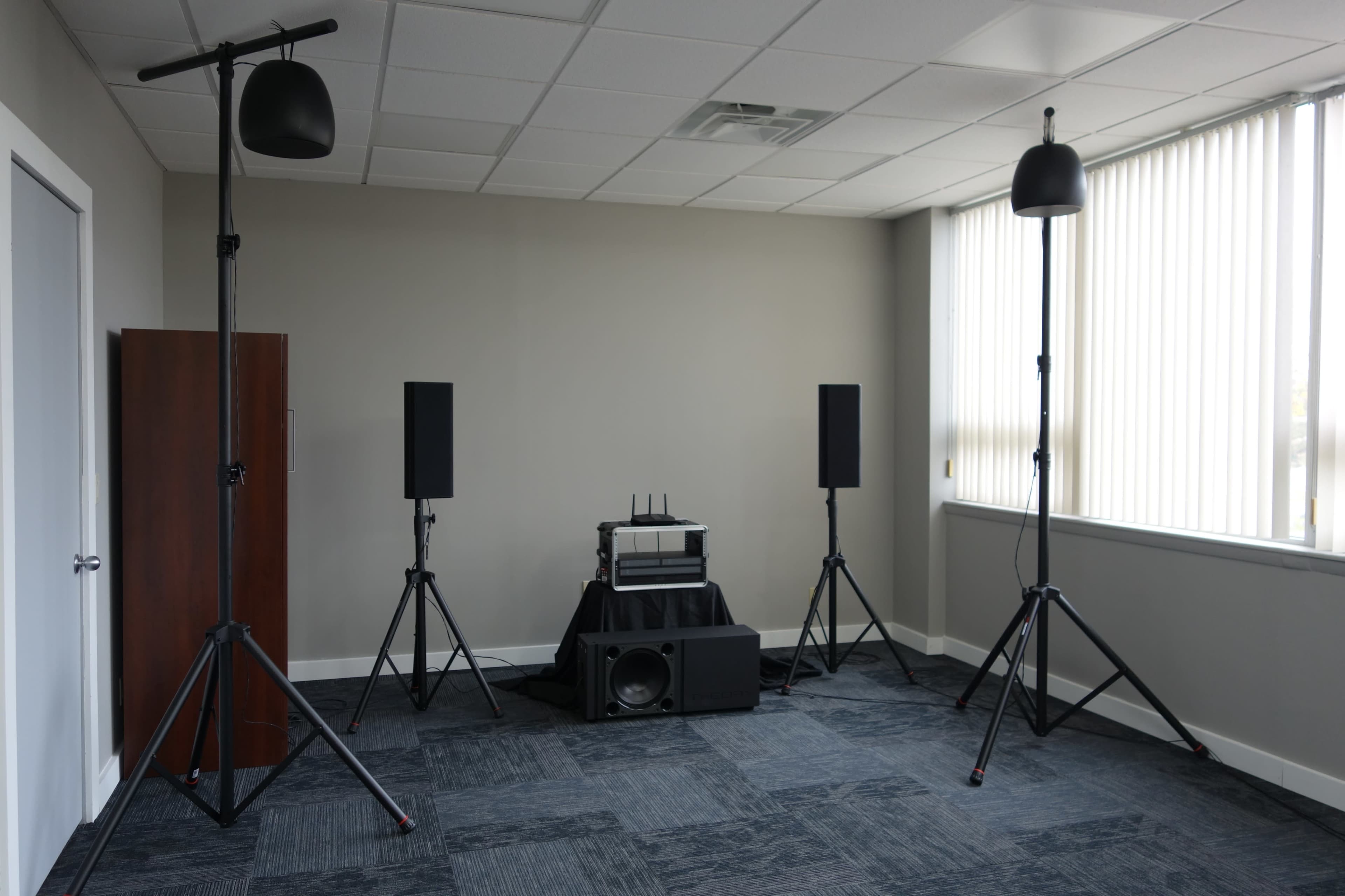 A room set up with audio equipment, including speakers on stands and a central sound system on a black table.