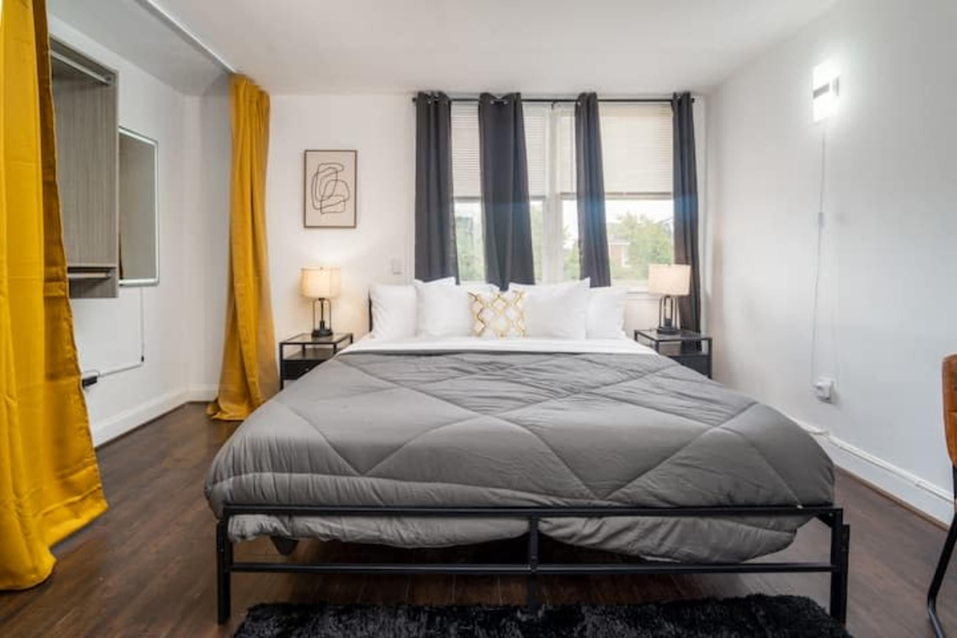A bedroom with a large bed, two bedside tables with lamps, and large windows dressed with black and yellow curtains.
