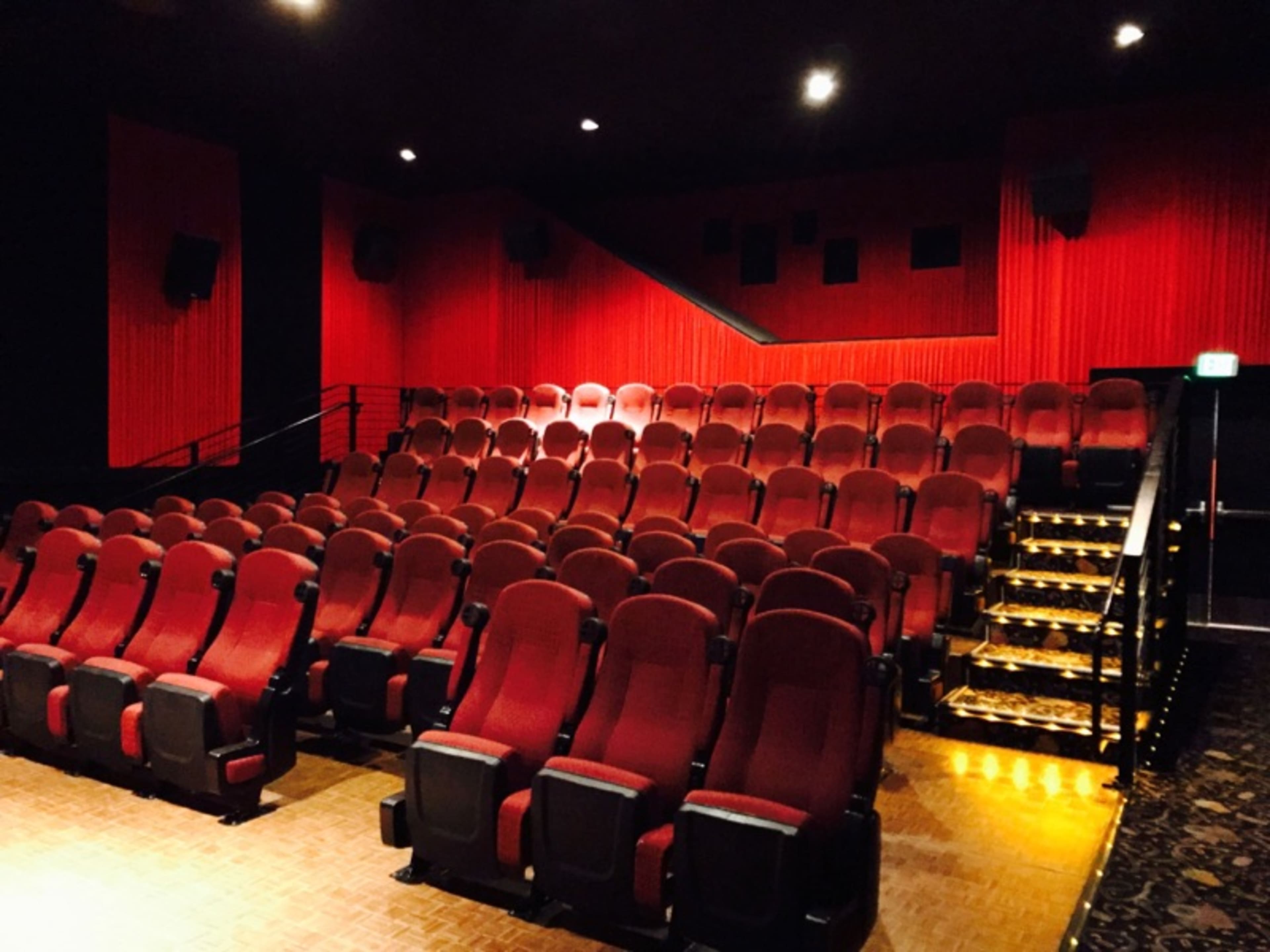 An empty theater with red velvet seating arranged in rows and a staircase at the back.