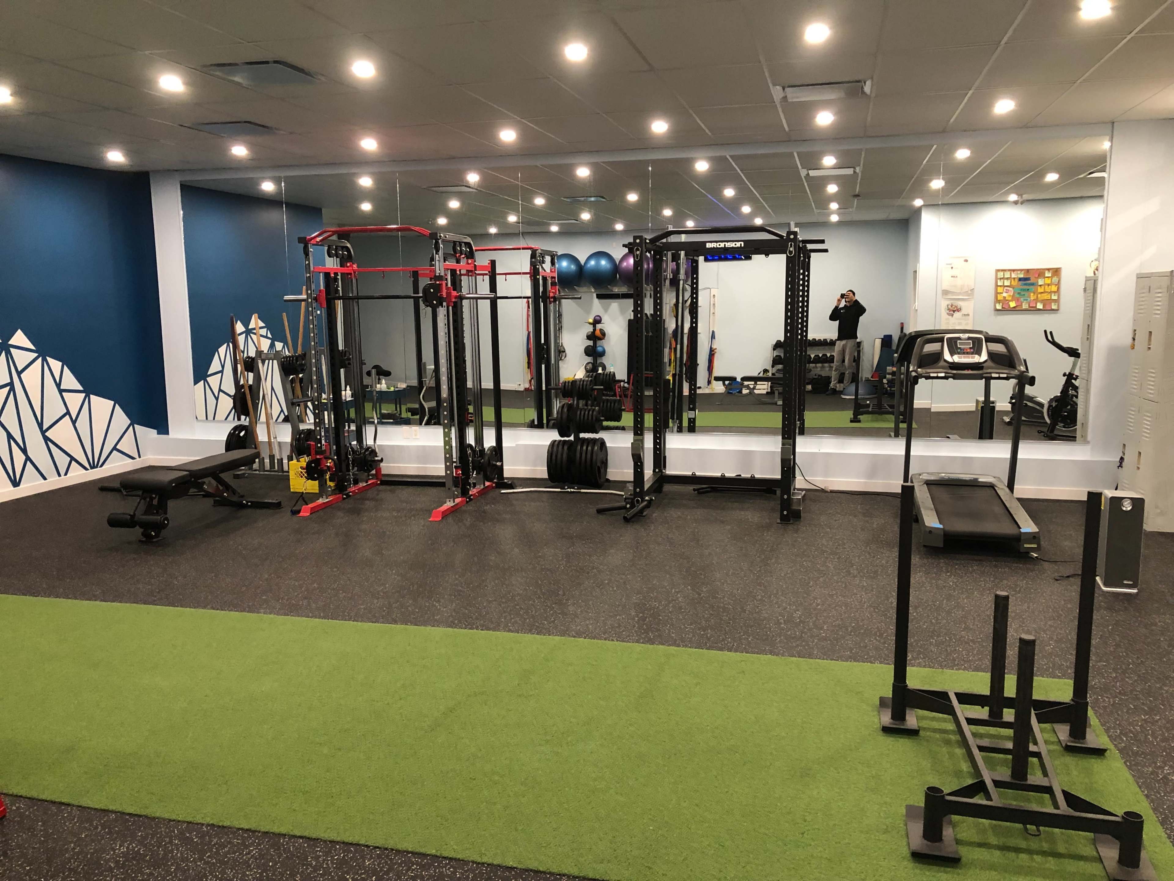 The gym features workout equipment including free weights, a bench, and a treadmill on a green turf floor.