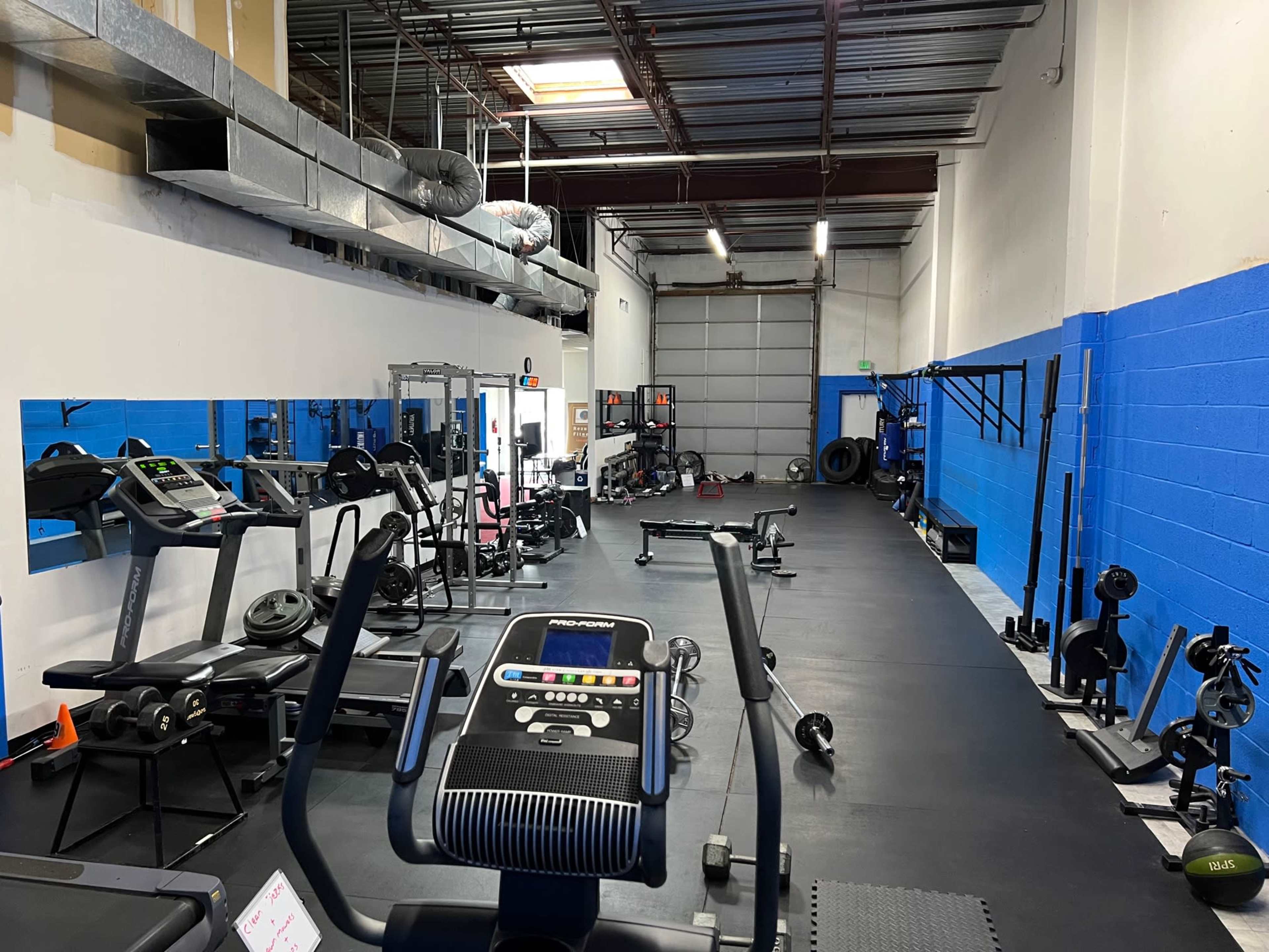 A fitness gym with various exercise equipment arranged along the walls, including treadmills, weights, and resistance machines.