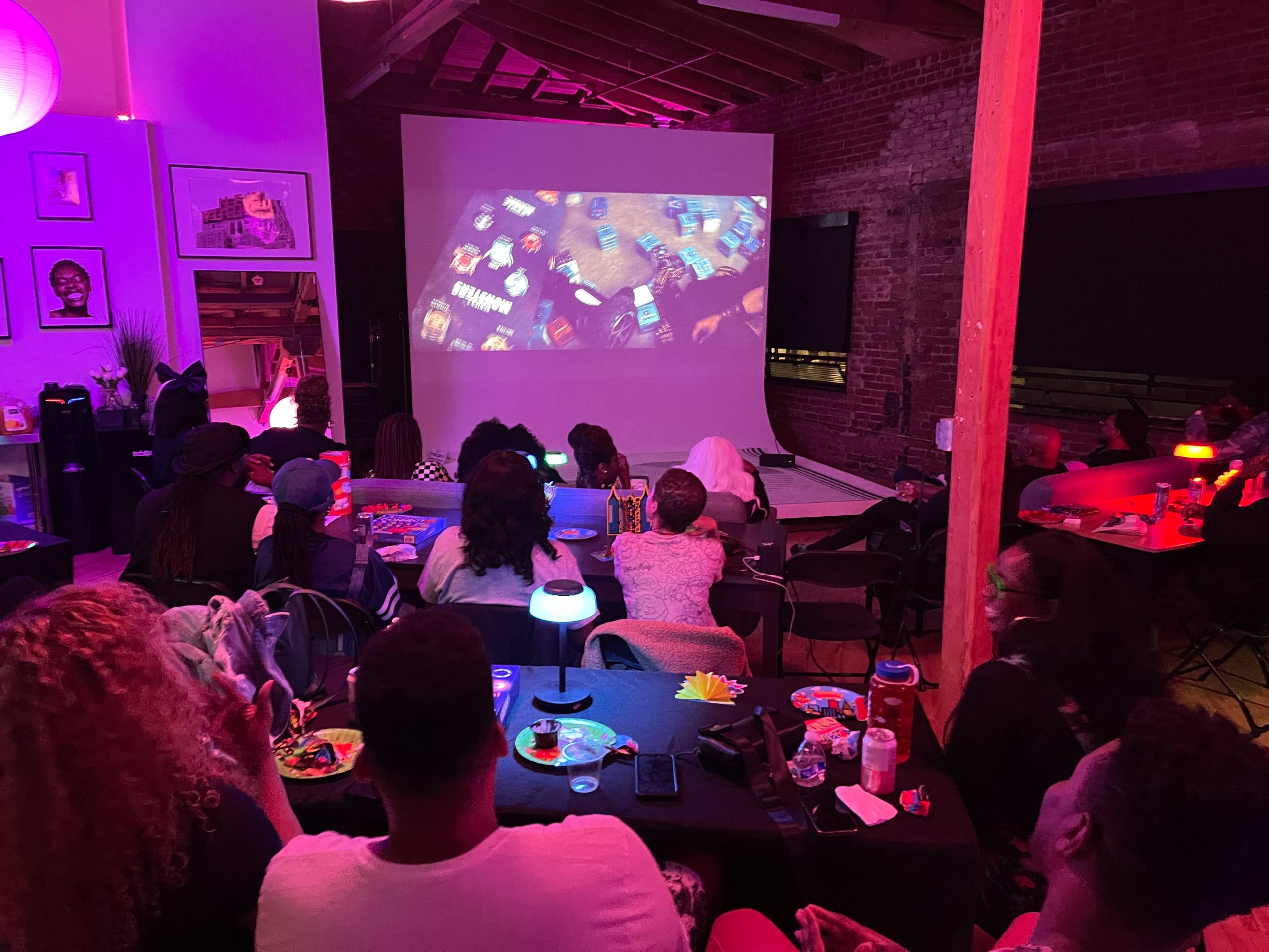 A group of people sit in a dimly lit room watching a film projected on a large screen.