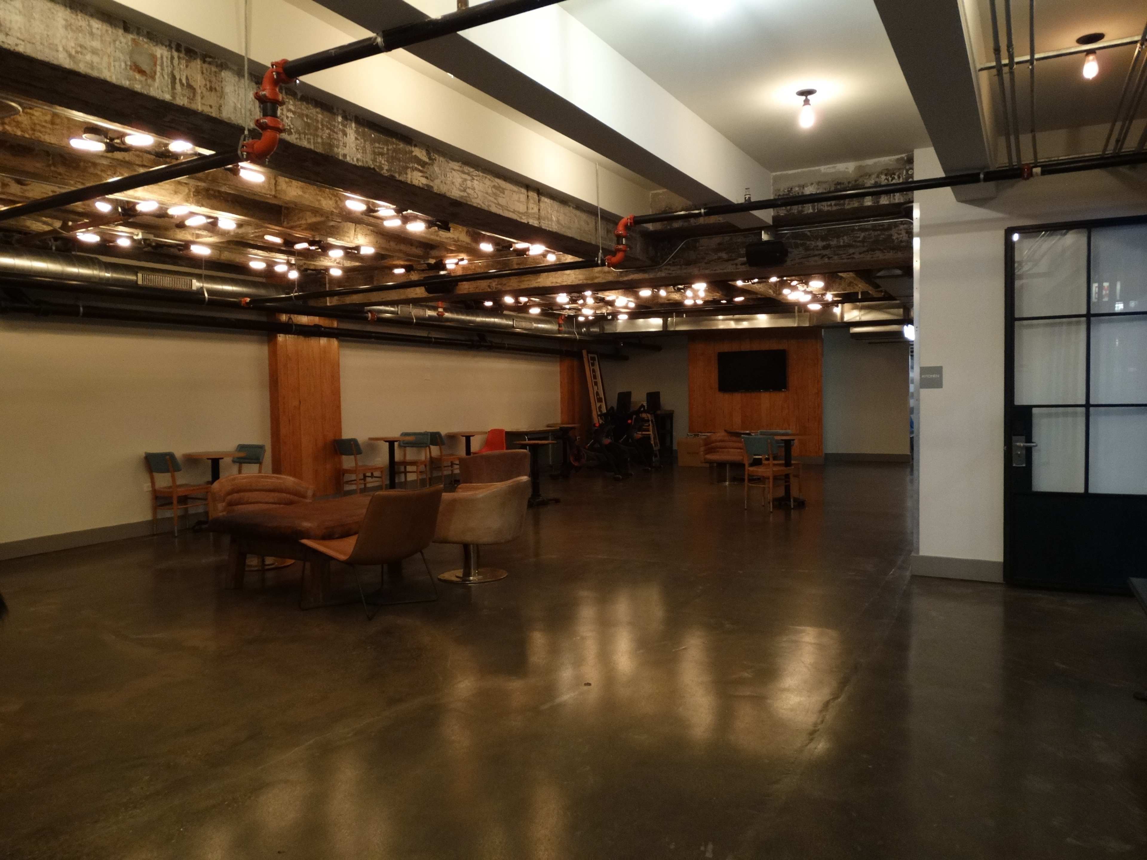 An industrial-style interior space with exposed beams, a concrete floor, and various seating arrangements.
