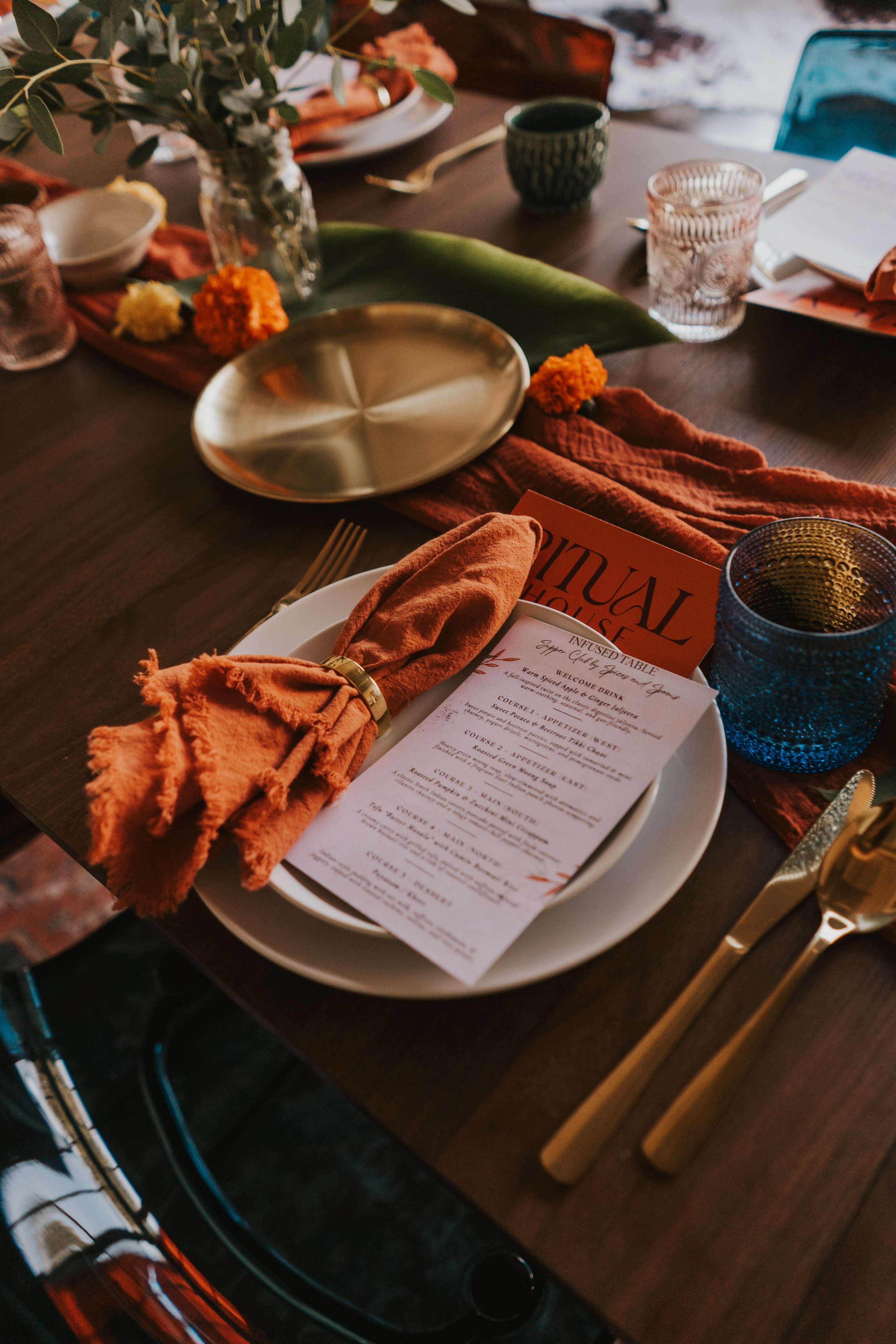 A beautifully arranged dining table features plates with decorative napkins, menus, and colorful centerpieces.