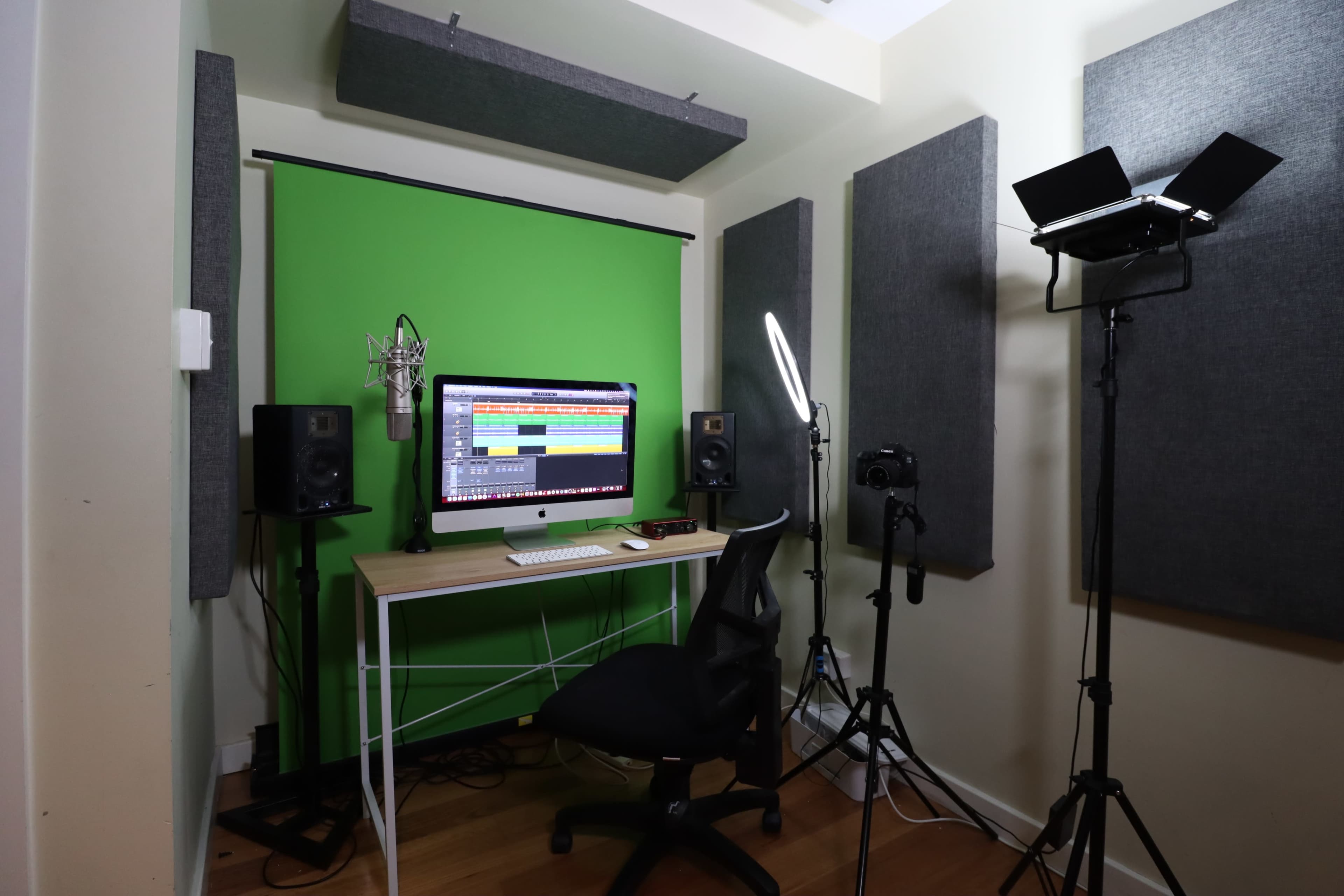 The image shows a small music recording studio with a green backdrop, a computer setup, microphones, speakers, and lighting equipment.