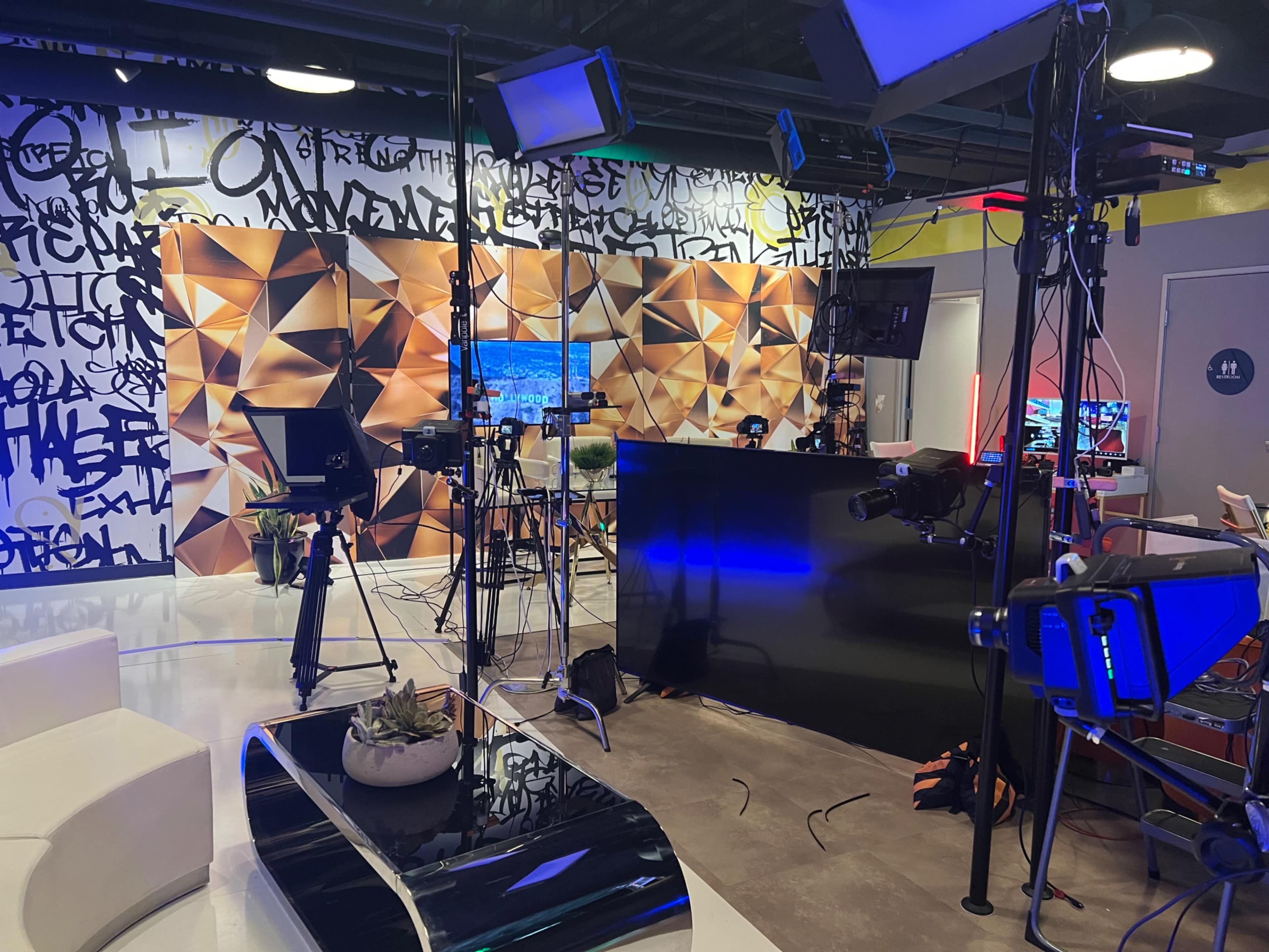 A modern studio setup with multiple cameras, lighting equipment, and a decorative backdrop featuring abstract geometric patterns and graffiti.