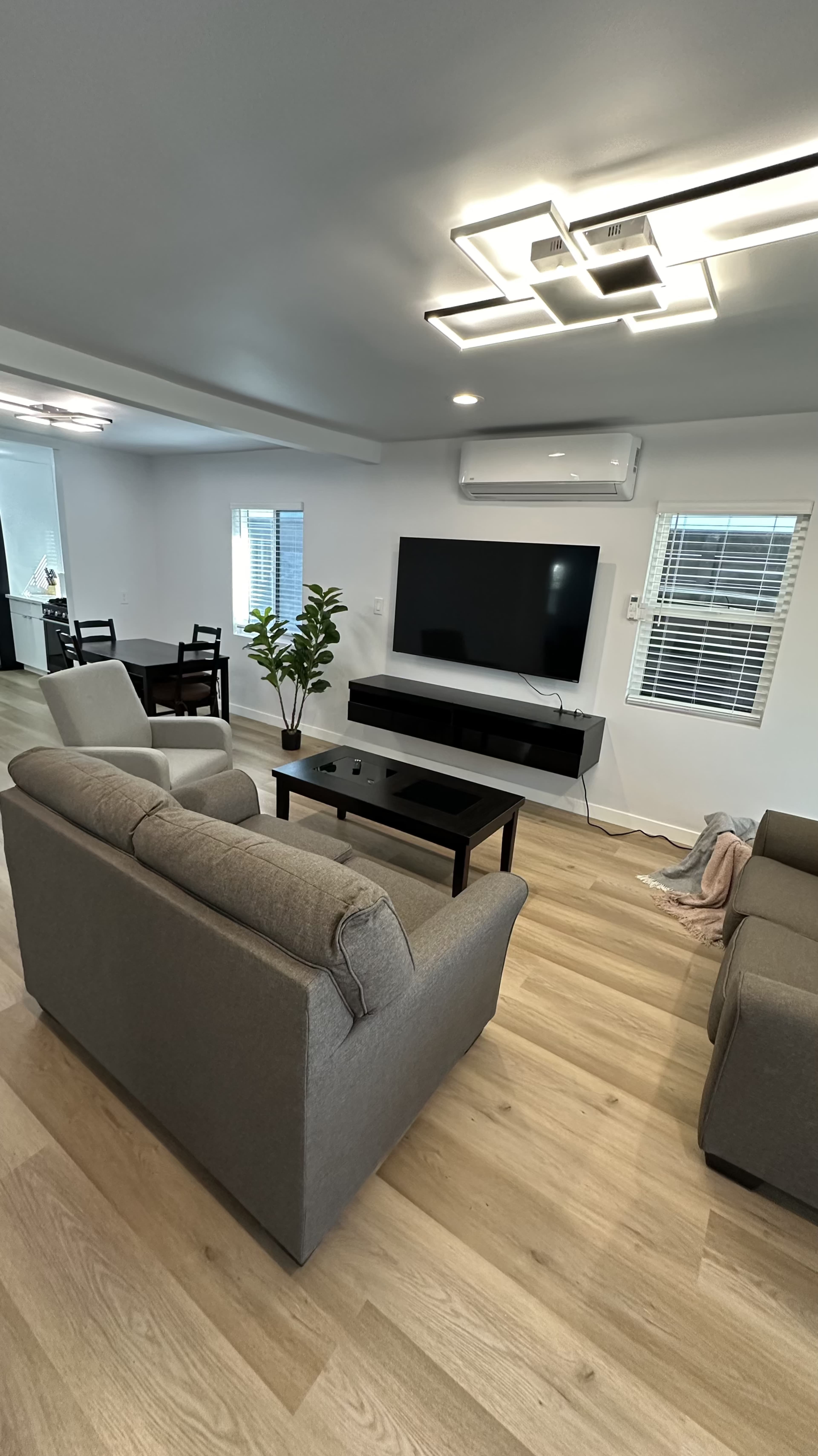 A modern living room with two gray sofas, a black television stand, and a wall-mounted TV, all set on light wooden flooring.