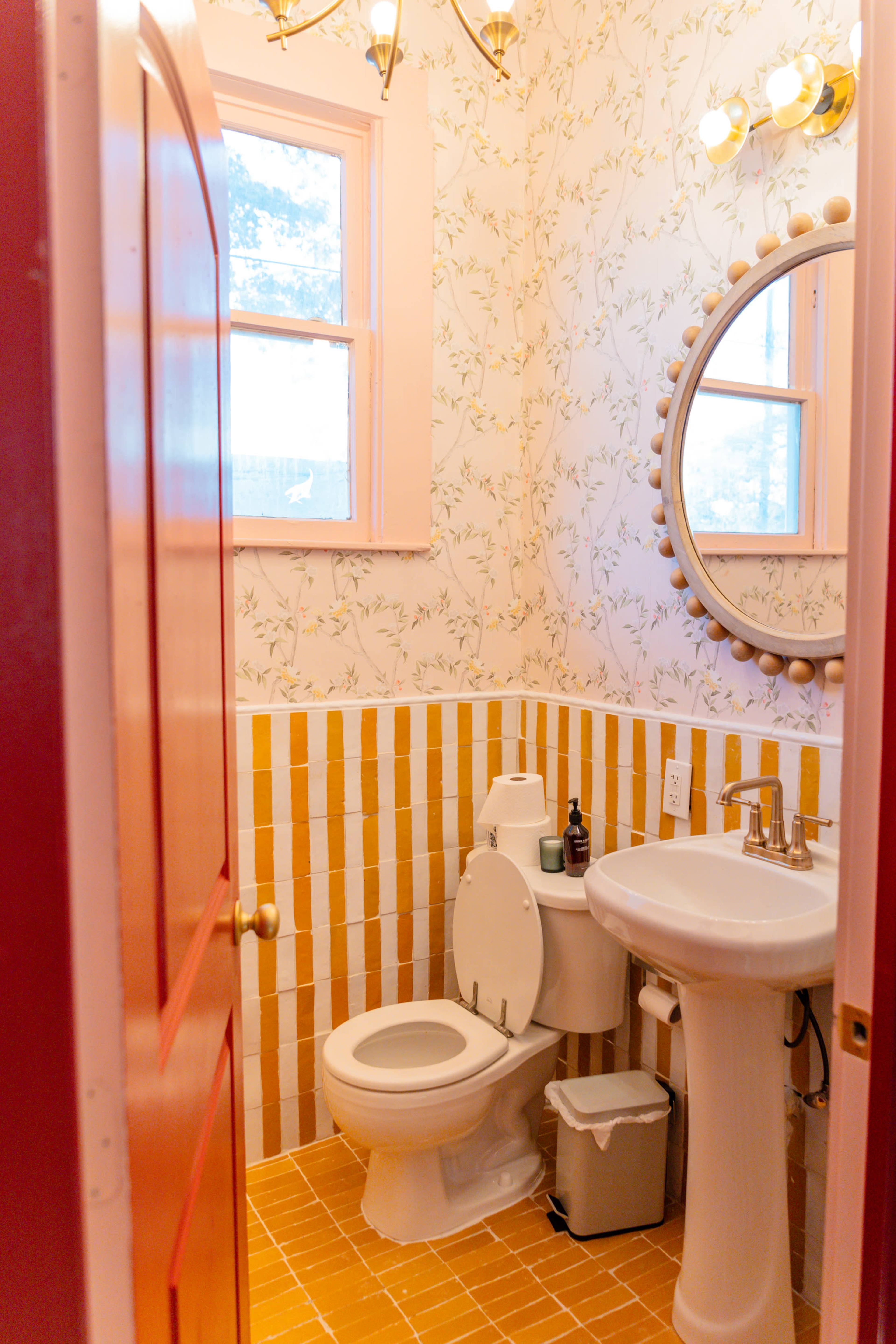 The bathroom features yellow and white tiled walls, a round mirror above the sink, and a closed toilet next to the door.