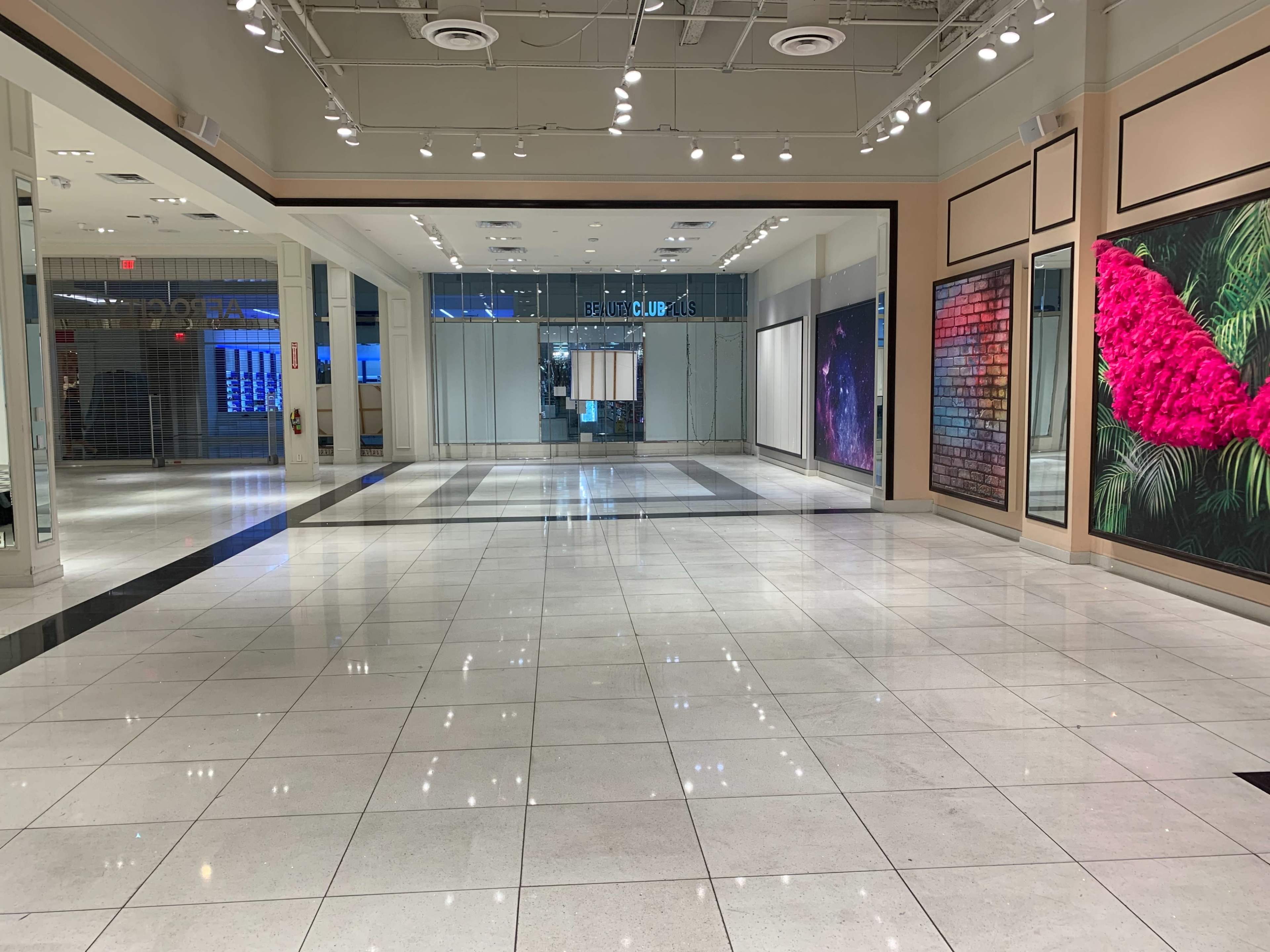 A spacious, brightly lit retail area with polished tile floors, showcasing large, colorful wall displays and an entrance to a closed store in the background.