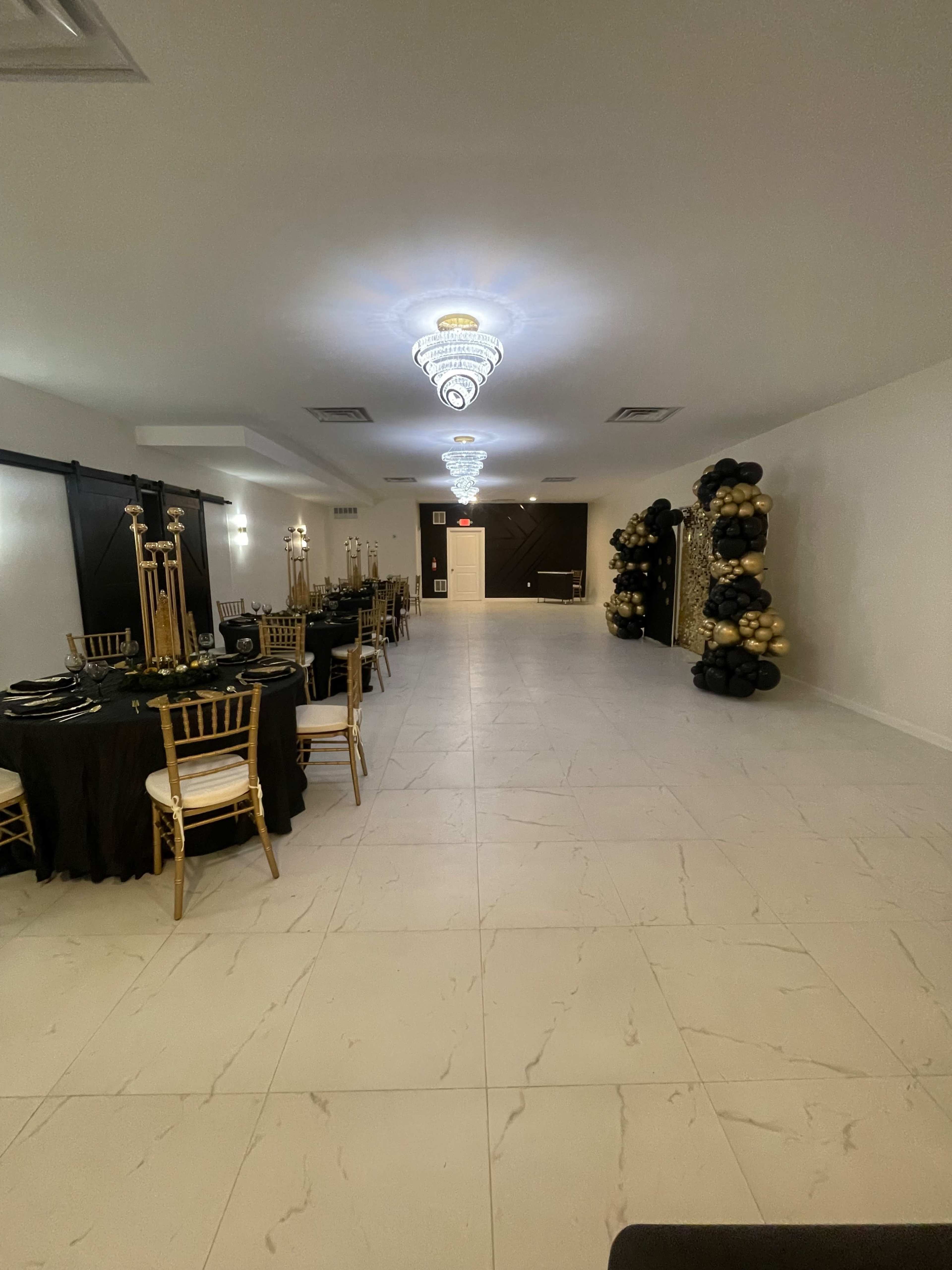 The image shows an elegant event space featuring black and gold decor, tables set with black tablecloths, and a decorative balloon arrangement on one side.