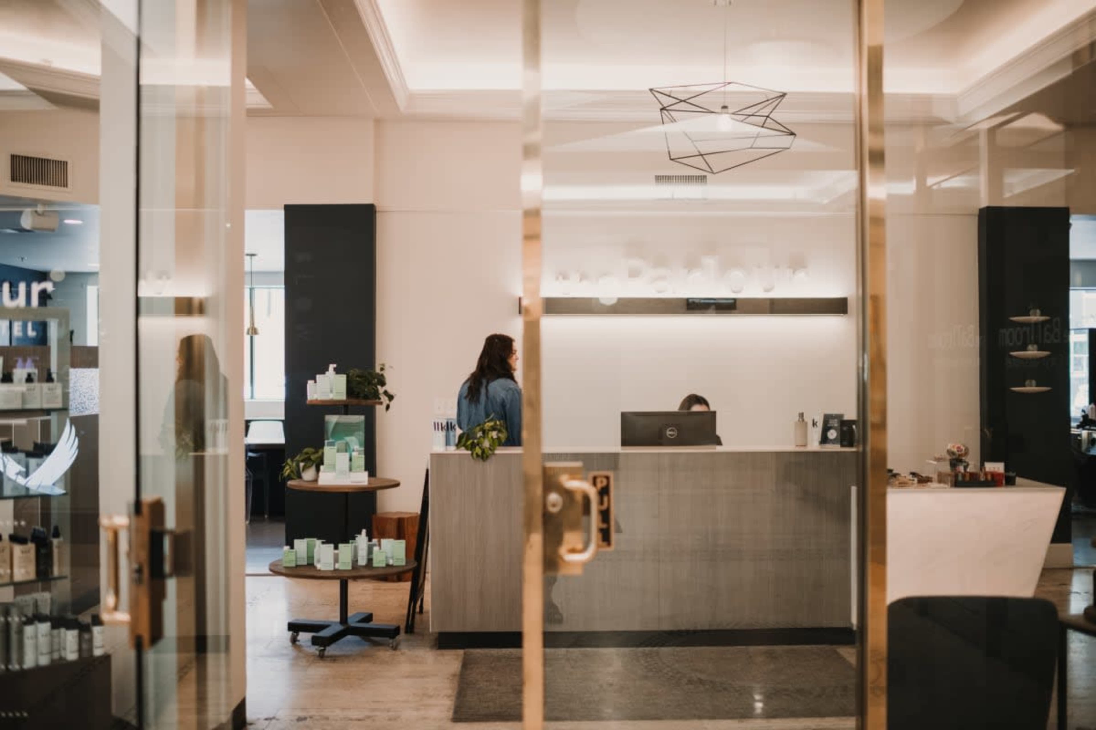 A modern reception area with a front desk, seated staff, and various skincare products displayed on shelves.
