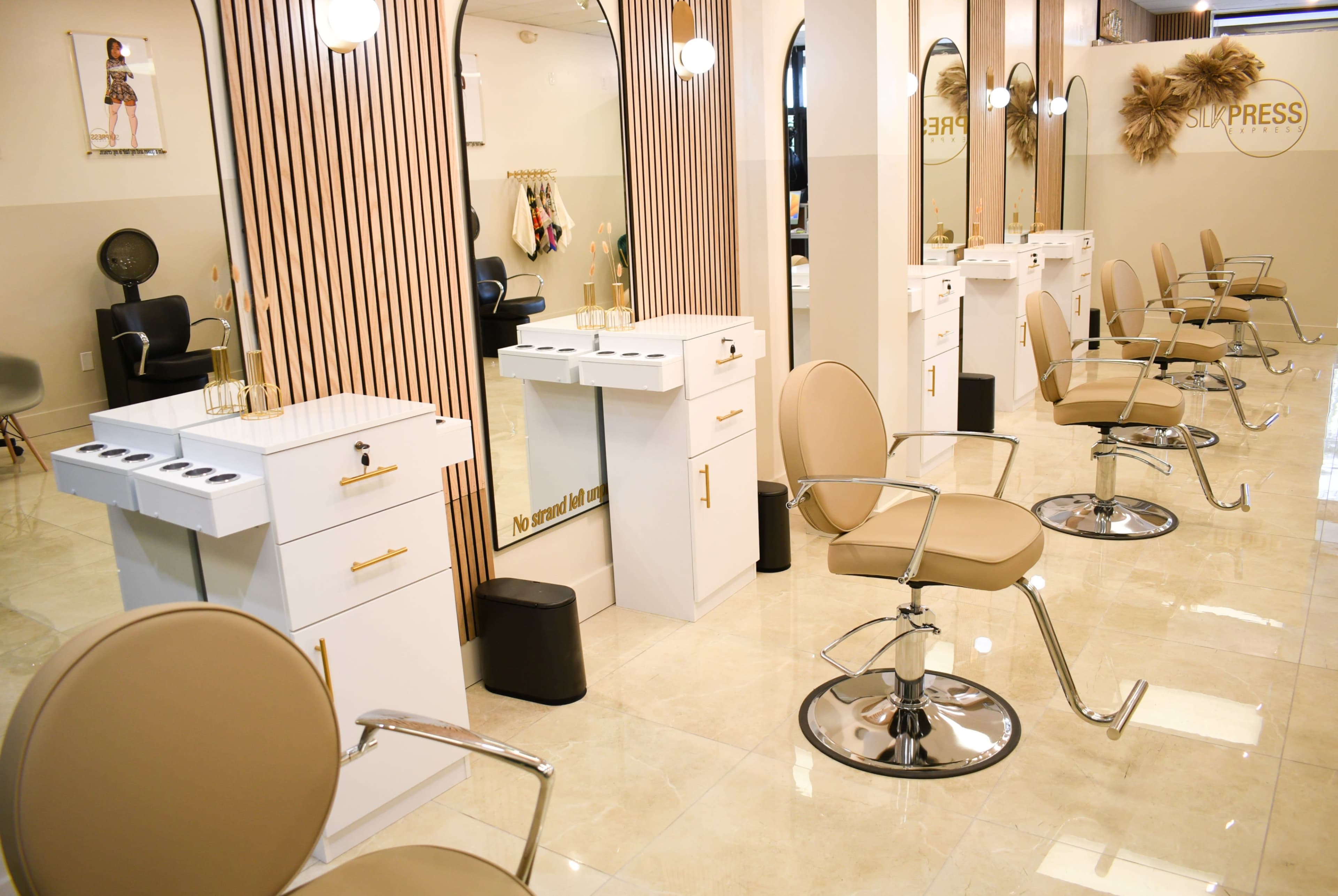 A modern hair salon with white cabinetry, beige chairs, and wooden paneling along the walls.