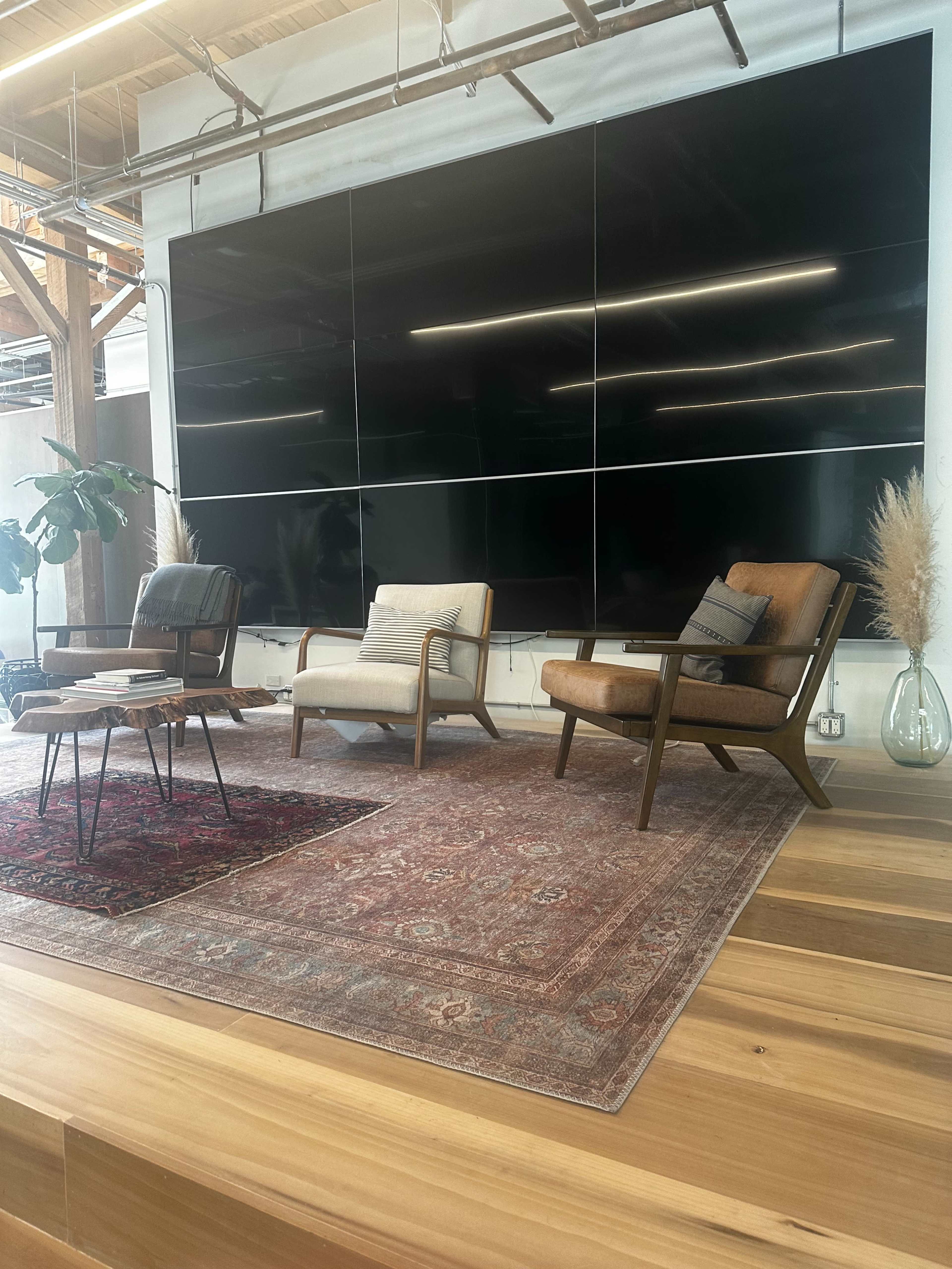 A room features two chairs and a coffee table on a rug, with a large black screen on the wall and wooden flooring.