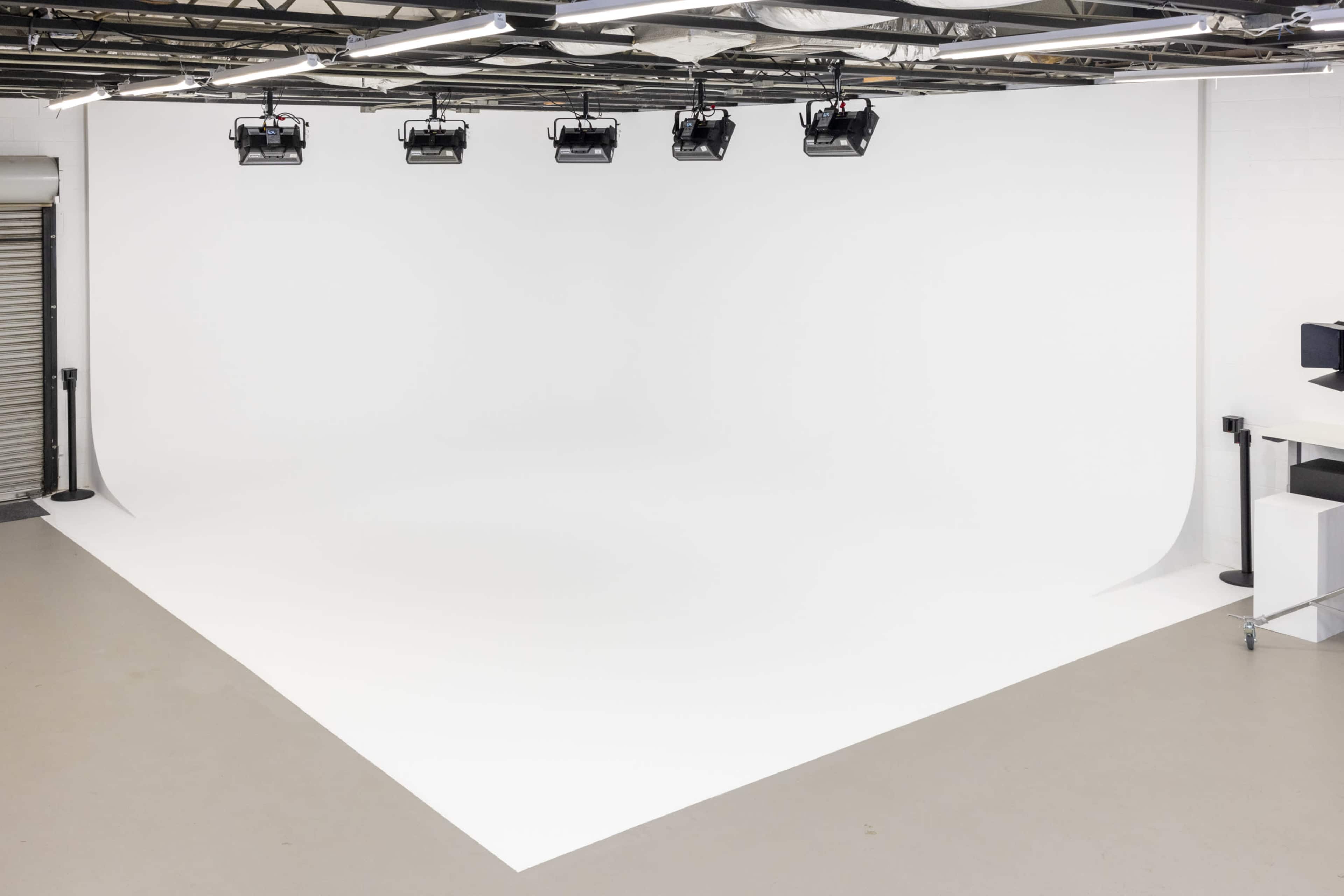 The image shows a photography studio with a seamless white backdrop, overhead lights, and a clean, minimalist design.