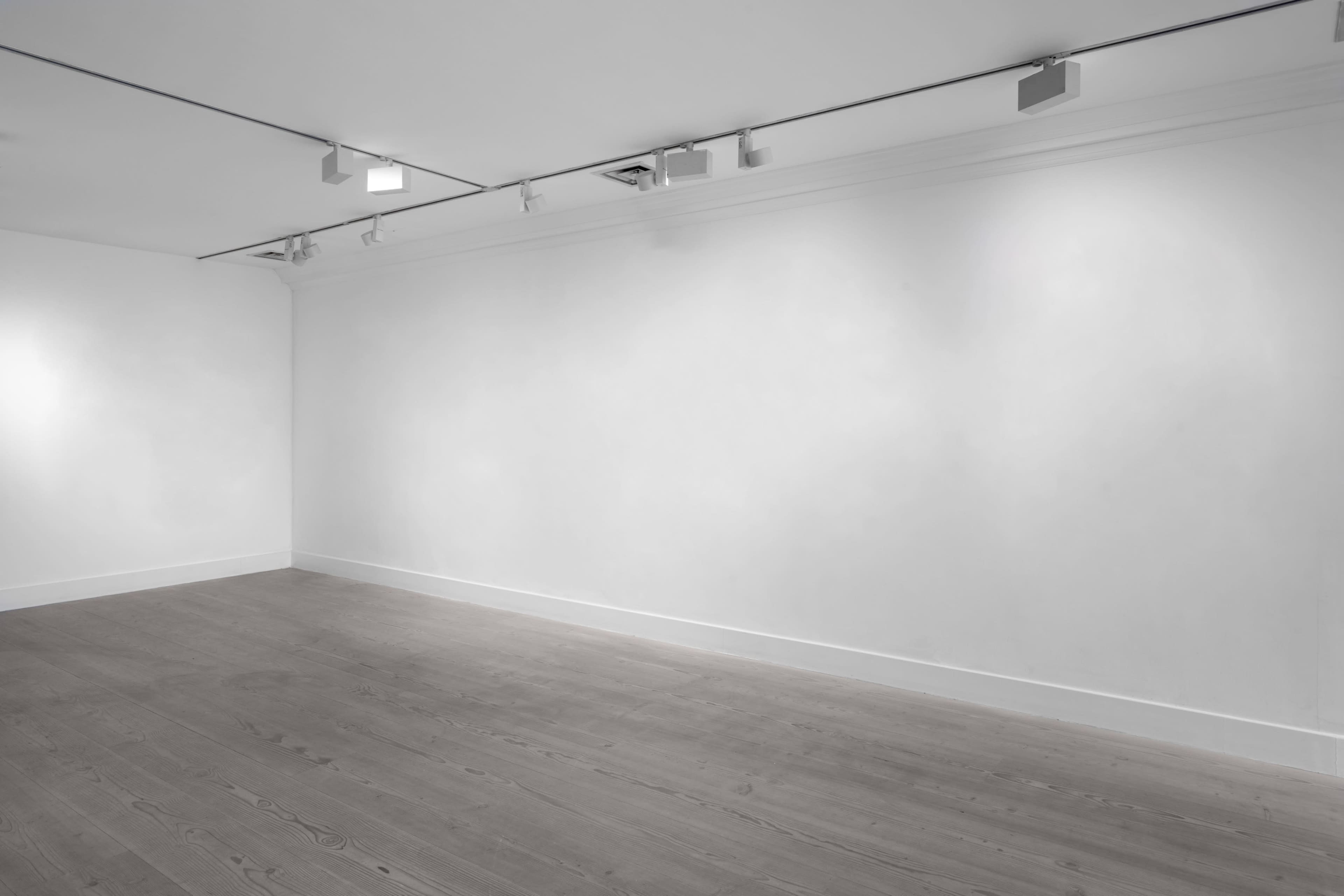 A spacious, empty art gallery with white walls and wooden flooring.