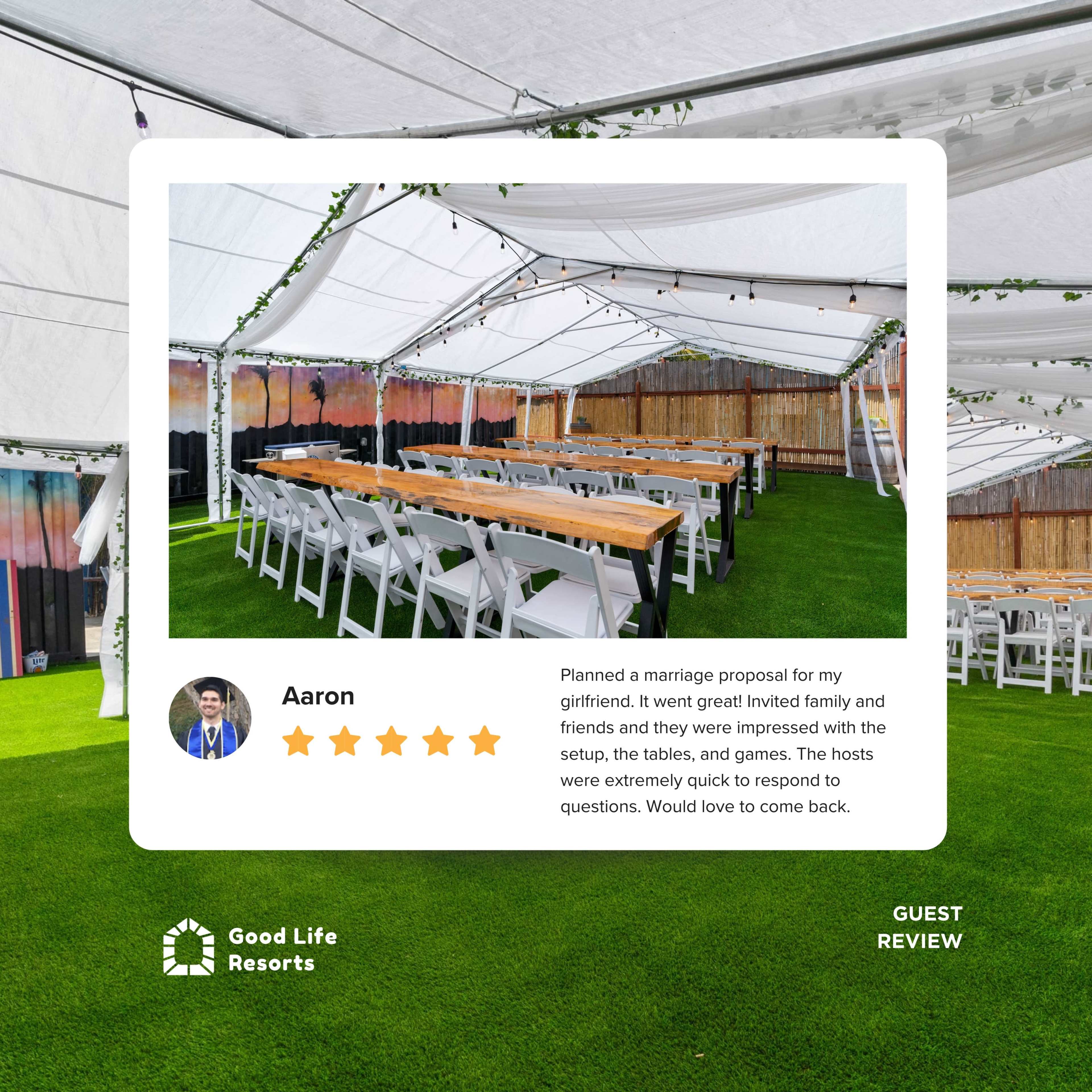The image shows an indoor event space with long tables set up under a canopy, surrounded by green grass and decorated with string lights.