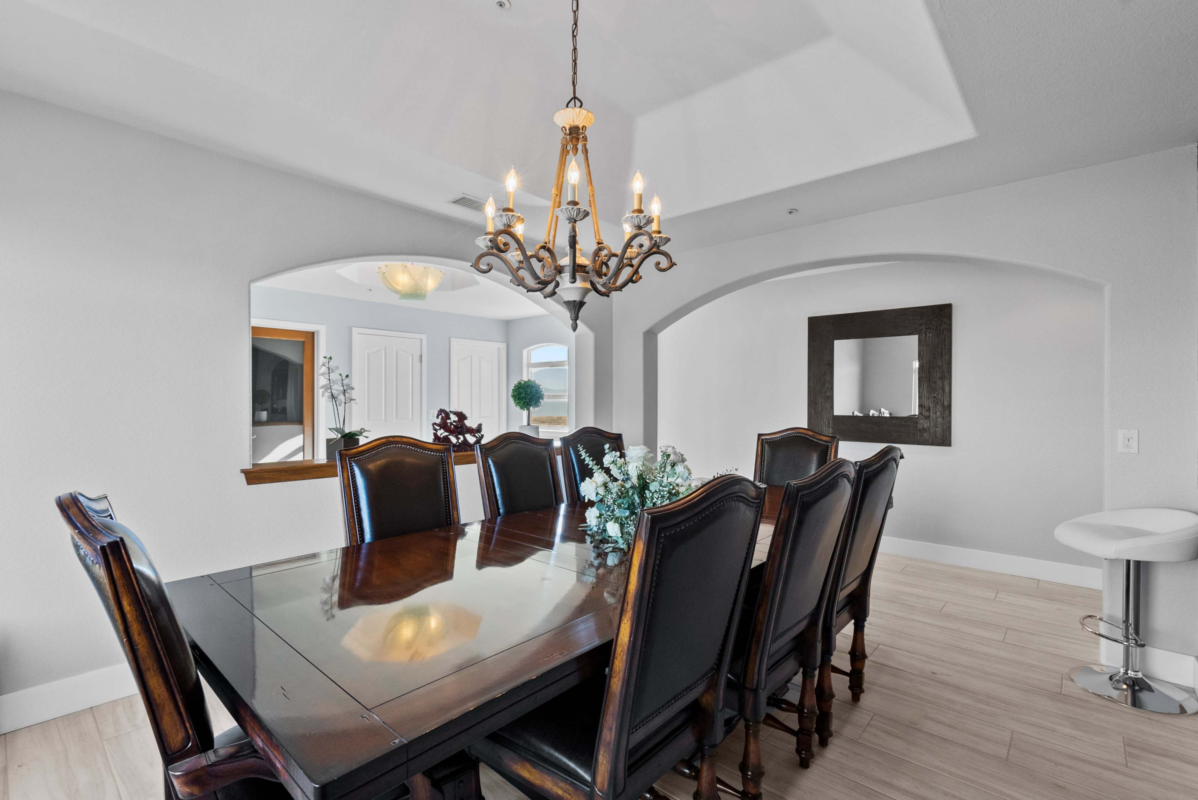 A dining room features a large wooden table surrounded by high-backed chairs, with a chandelier hanging above and a mirror on the wall.
