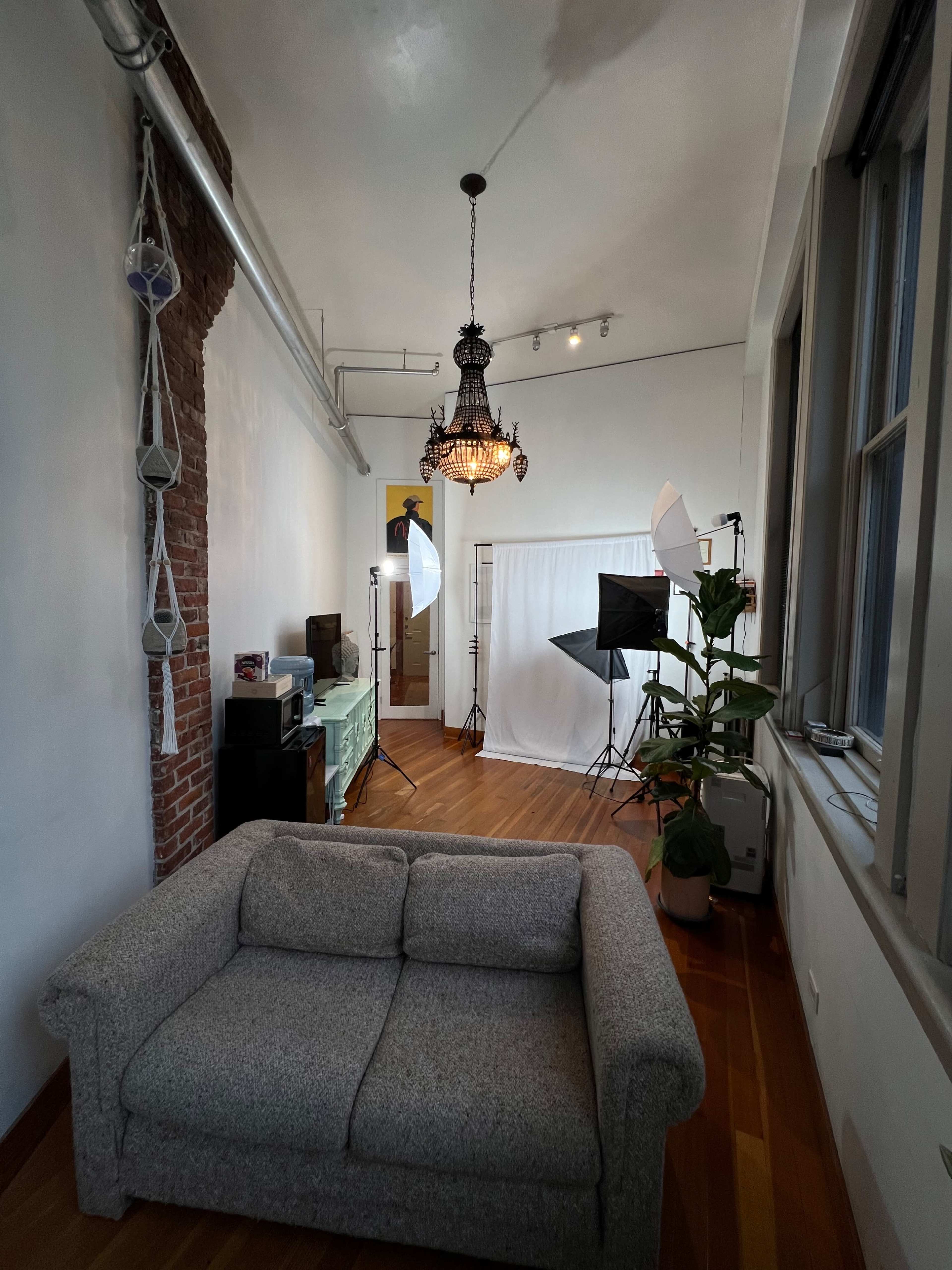 A bright room with a couch, a chandelier, and photography equipment set up against a backdrop.