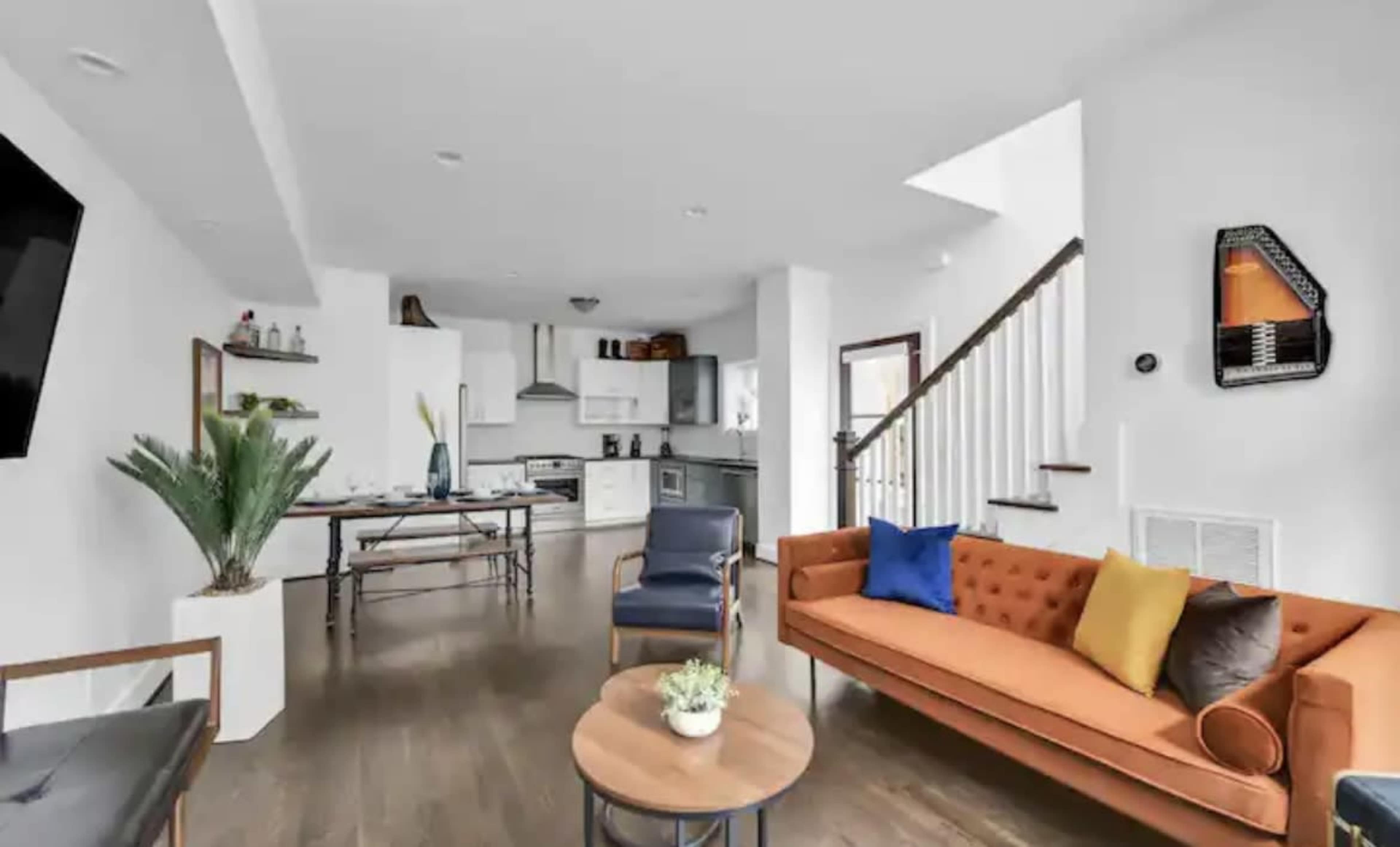 A modern living space featuring a bright open layout with a kitchen, a cozy orange sofa, and a wooden table.