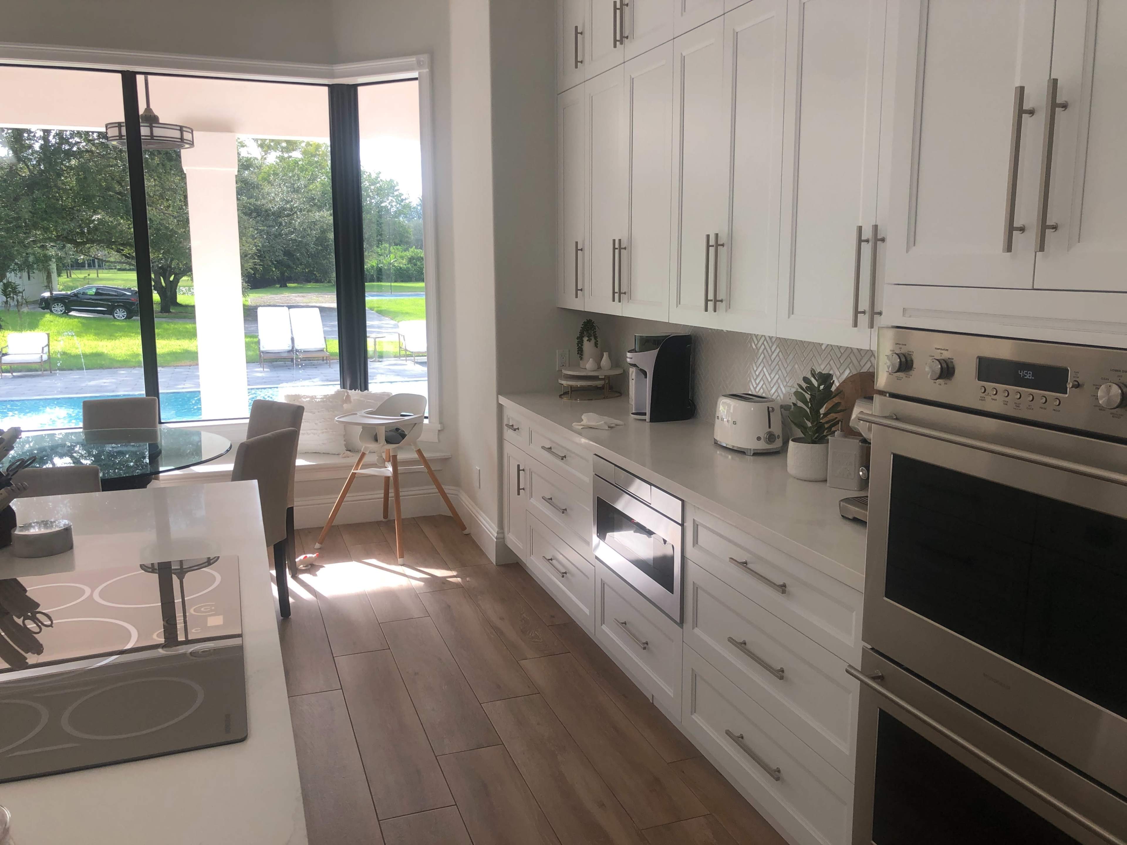 A modern kitchen featuring white cabinets, stainless steel appliances, and a view of a pool area through large windows.