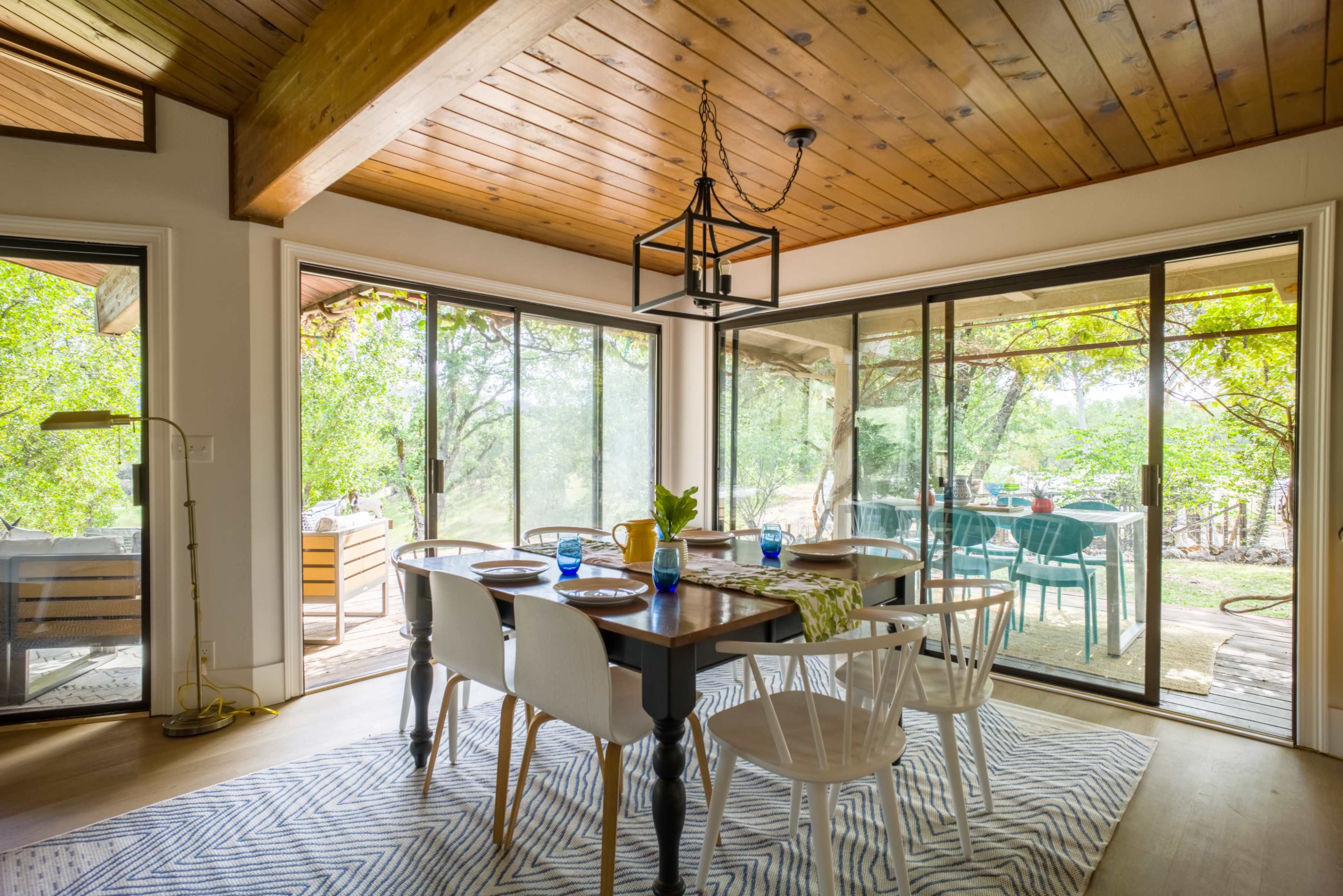 A dining area with a wooden table and white chairs is positioned near sliding glass doors that lead to an outdoor space.