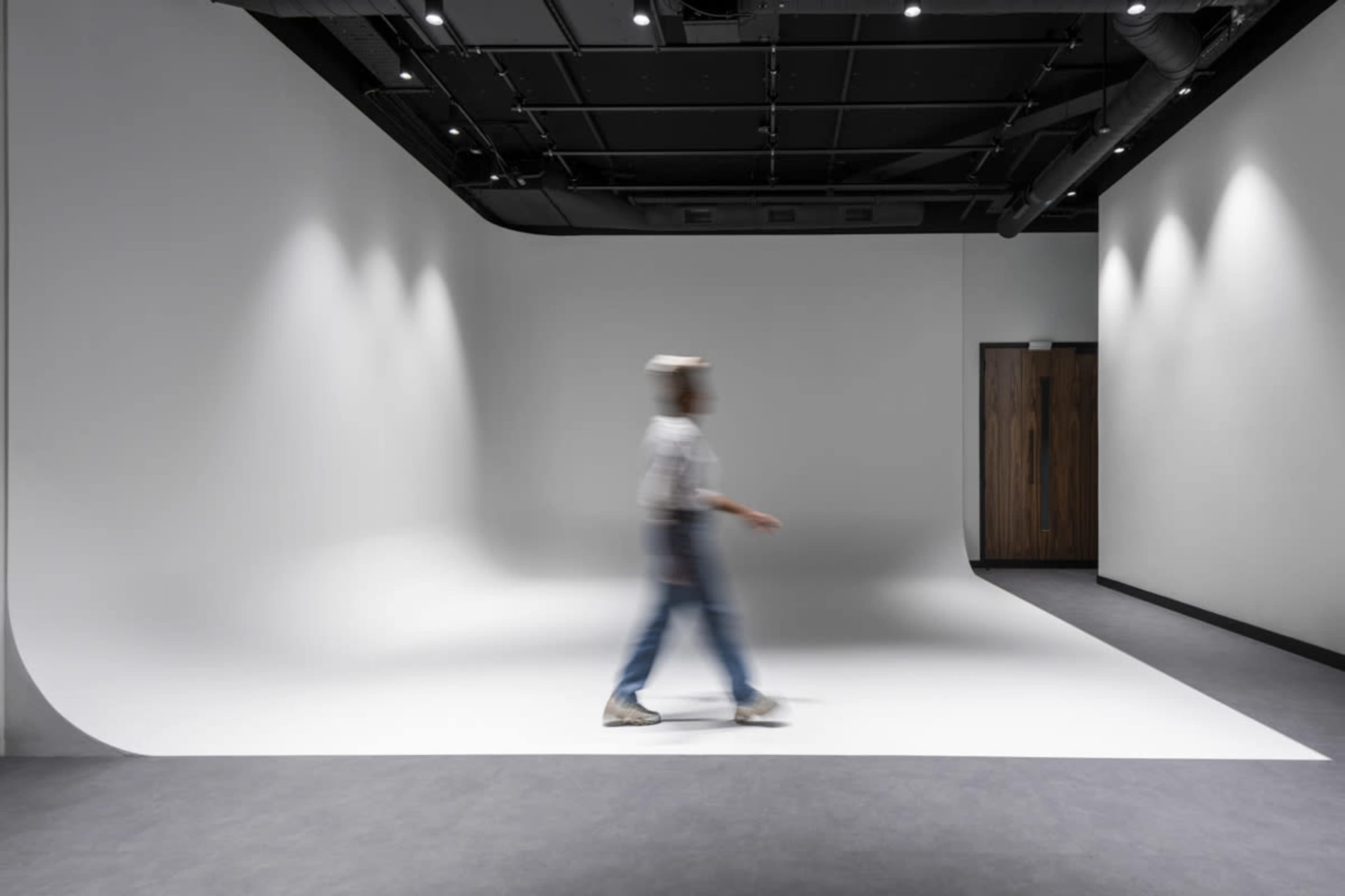 A person walks through a minimalist studio space with a curved white backdrop and dim lighting.