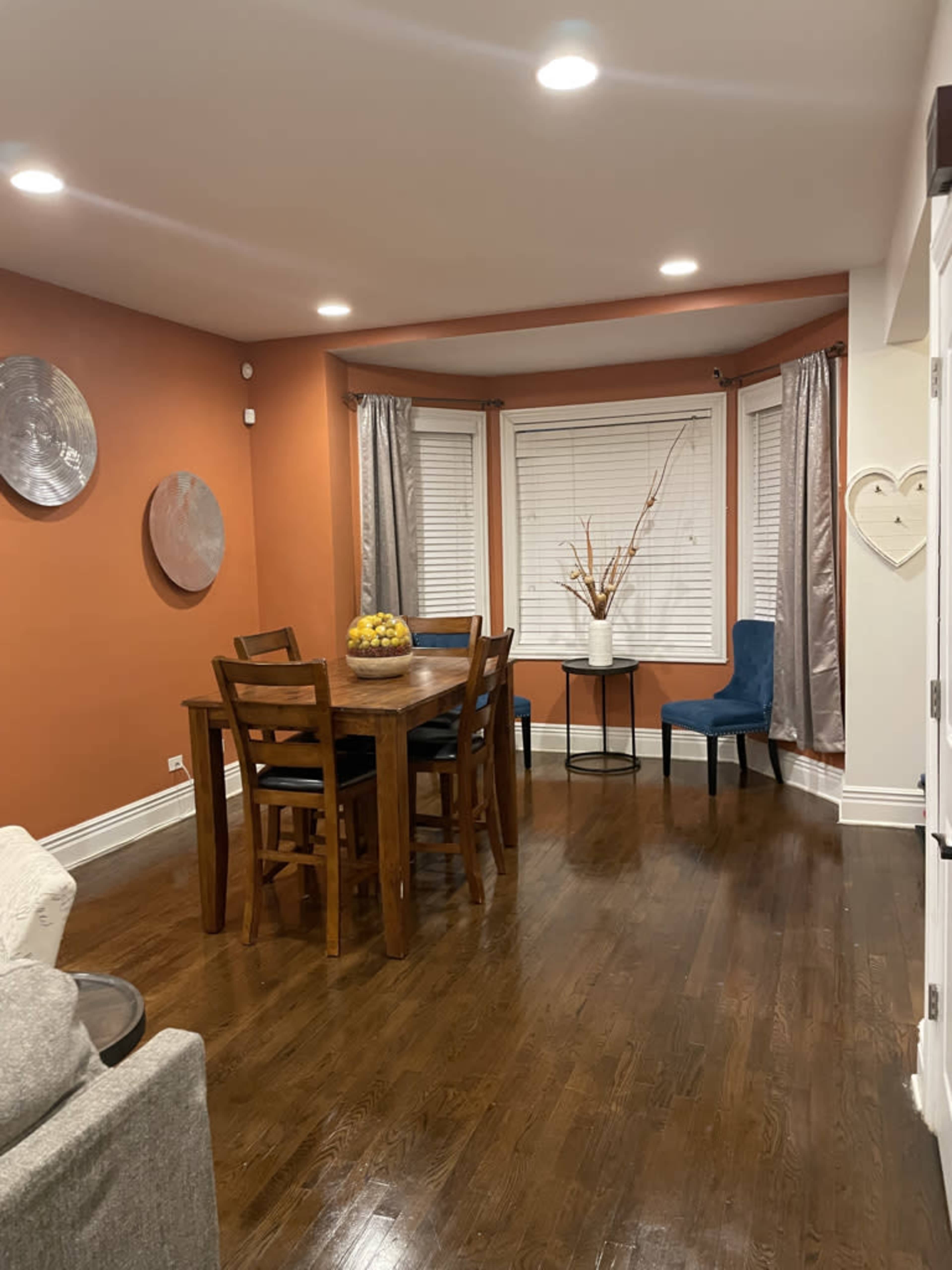 A dining area with a wooden table and chairs, surrounded by orange walls and window treatments.