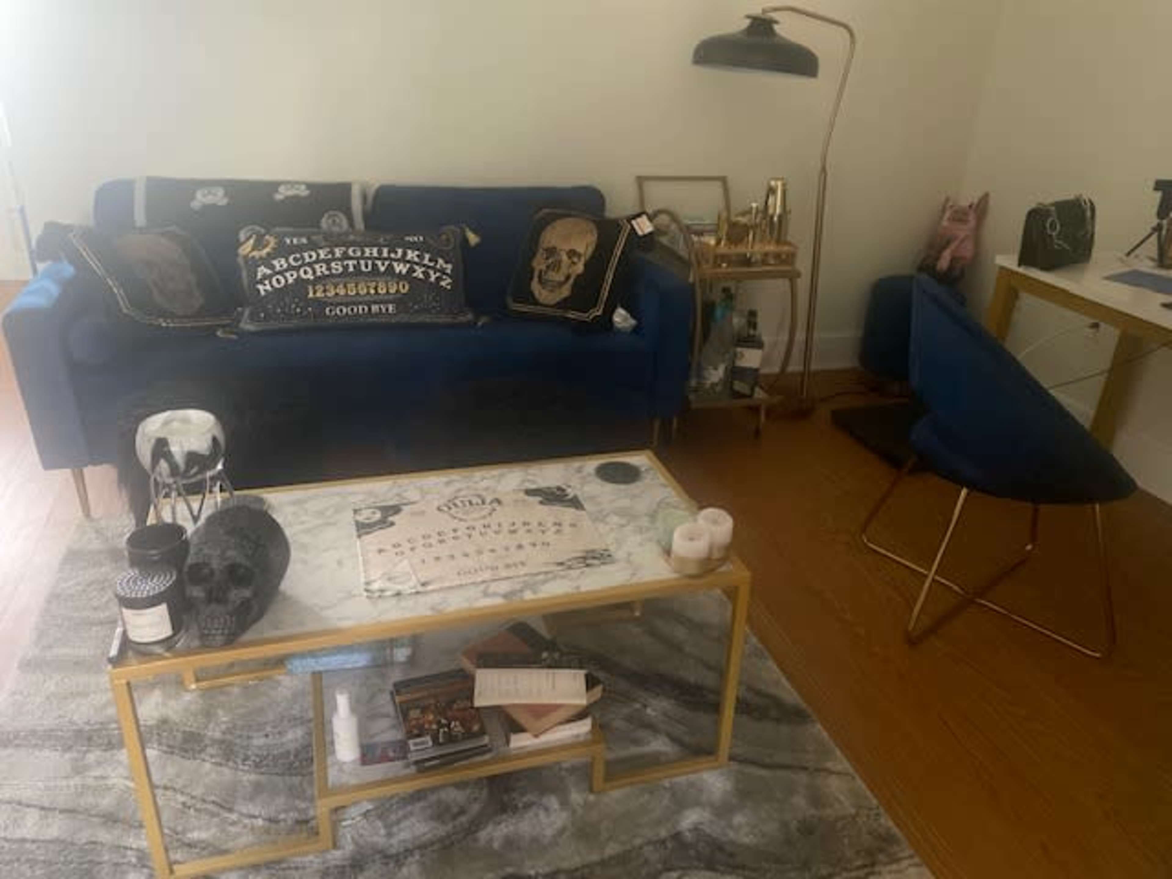 The image shows a living room with a blue sofa adorned with decorative pillows, a marble coffee table, and a small desk in the corner.