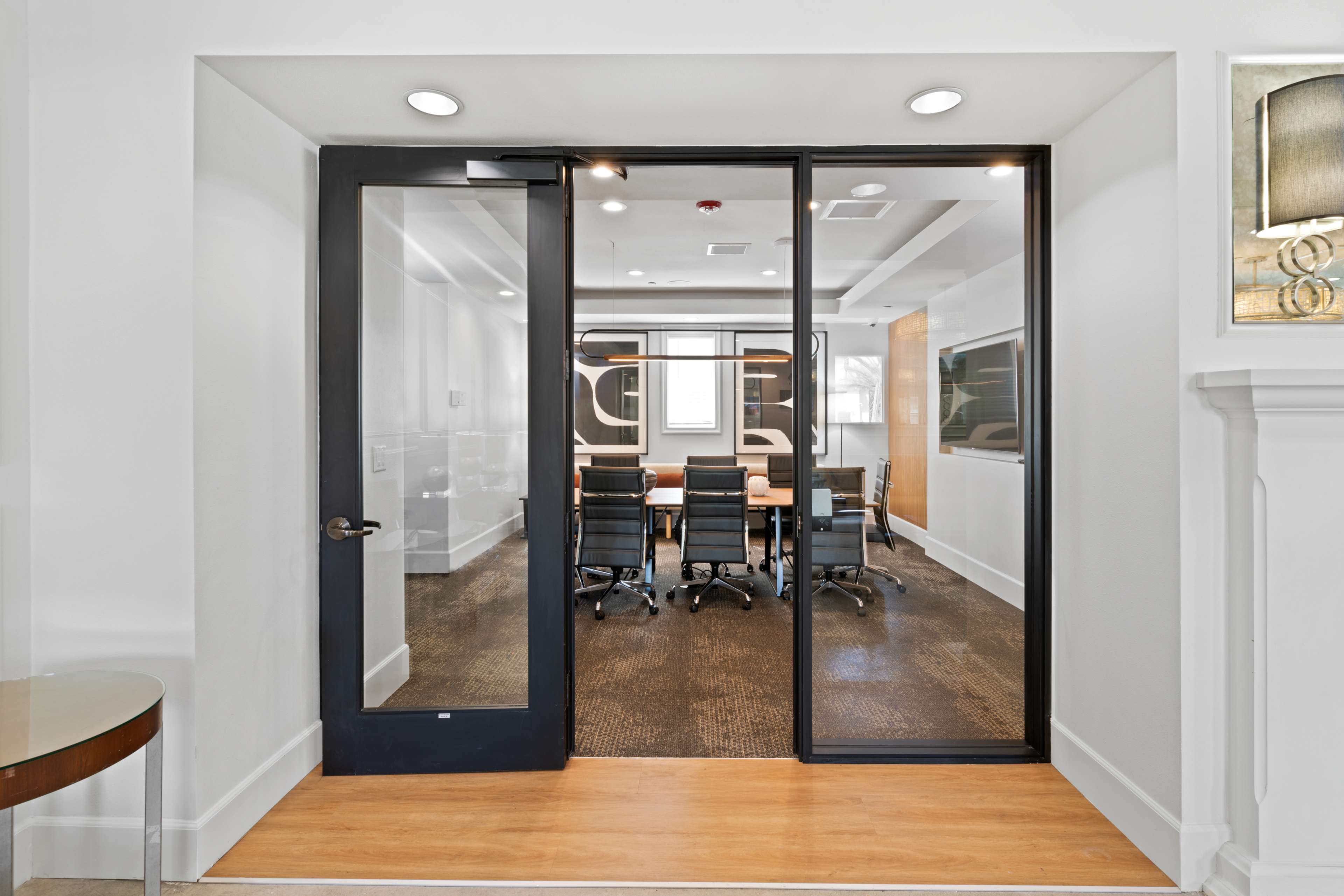 A glass-door entrance to a modern conference room featuring a long table and several black office chairs.