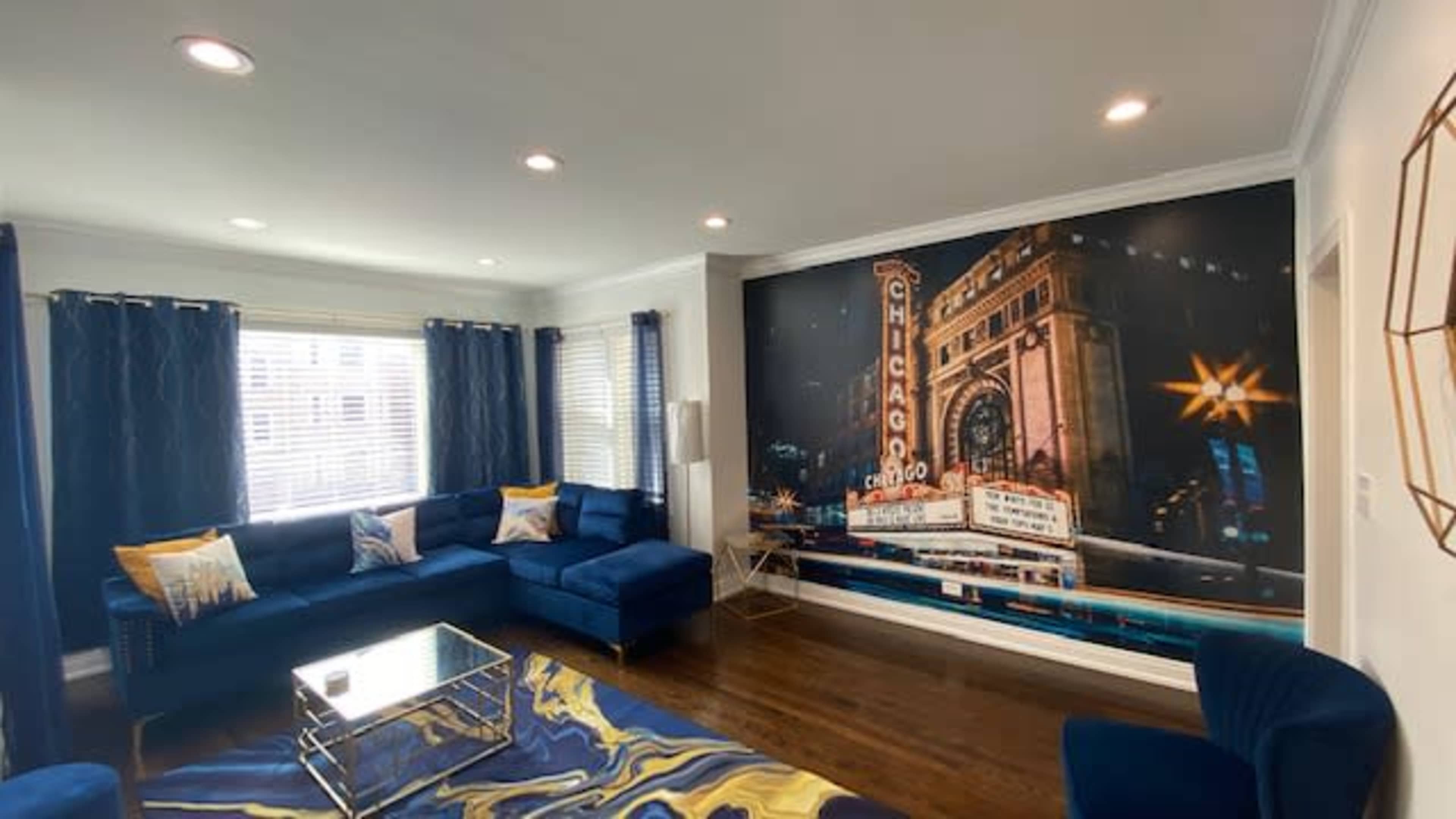 A modern living room features a large sectional sofa, a coffee table, and a mural of a vintage Chicago theater on the wall.